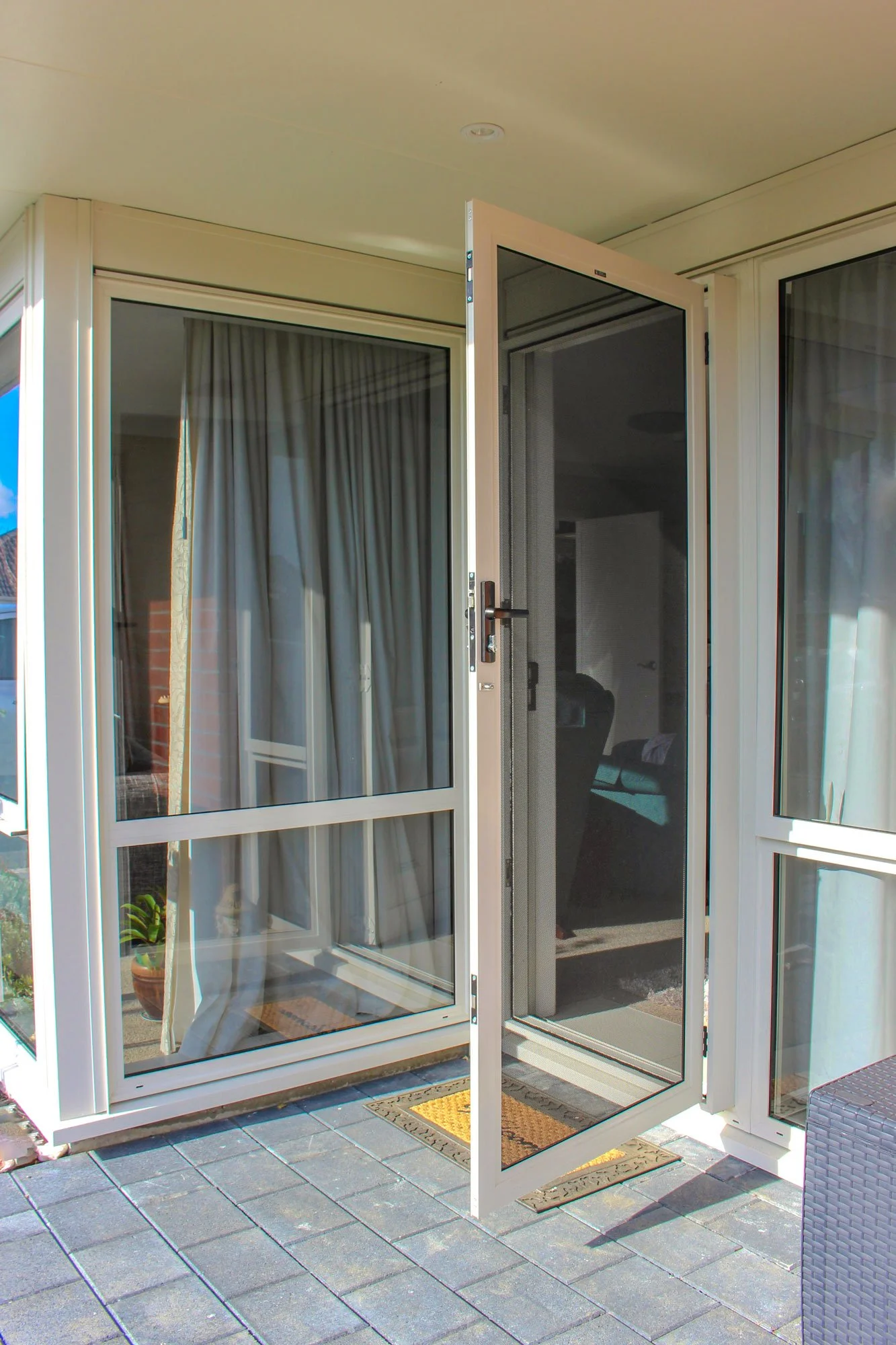 Open screened patio door beside glass windows on a tiled outdoor terrace