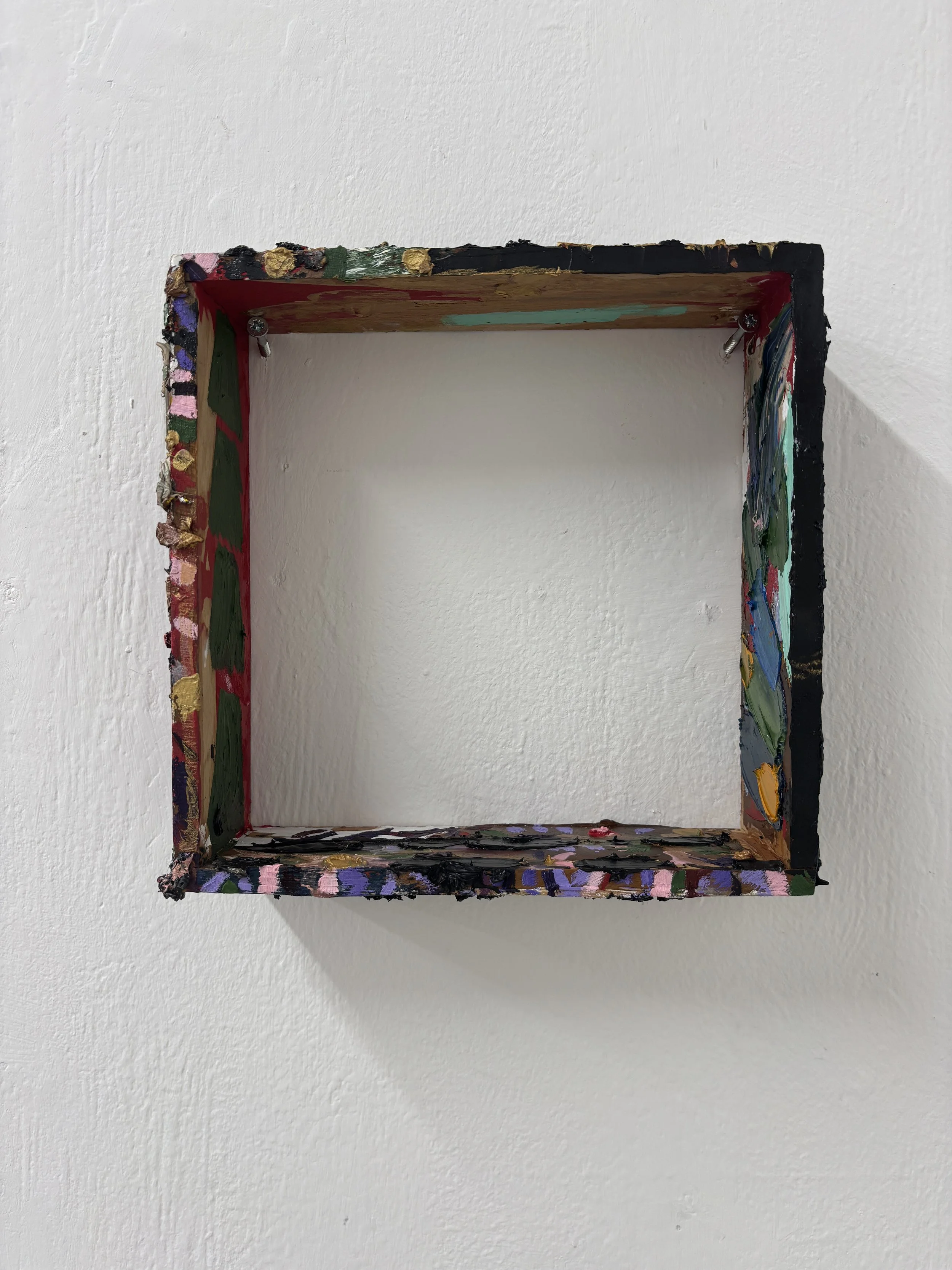 Empty wooden frame painted with colorful abstract brushstrokes, mounted on a white wall.