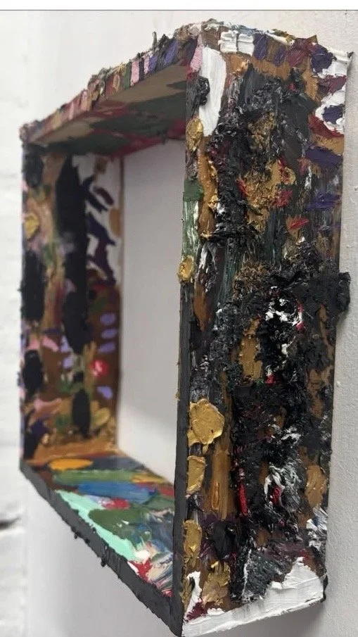 Three-dimensional painted picture frame with thick, textured brushstrokes of various colors, predominantly black, gold, and dark shades, creating an abstract, sculptural appearance.