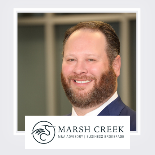 Business professional with a beard and mustache, smiling, wearing a dark suit and white shirt, standing outdoors in front of a building with blurred background, with the Marsh Creek logo and text at the bottom.