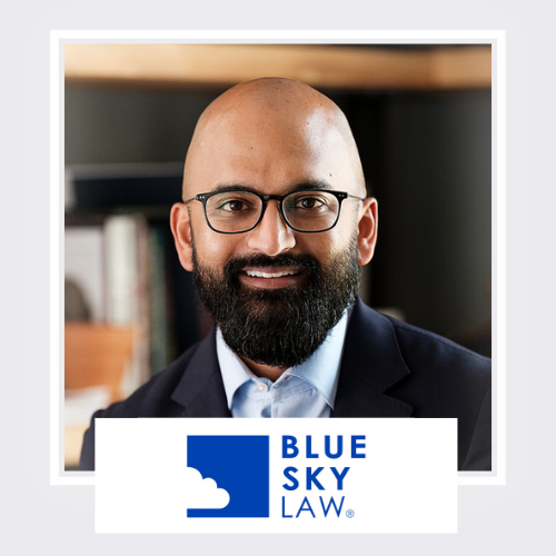 Portrait of a man with a beard and glasses, wearing a suit and smiling, with a 'Blue Sky Law' sign in front of him.