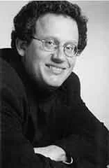 Black and white photo of a man with curly hair and glasses, smiling at the camera.