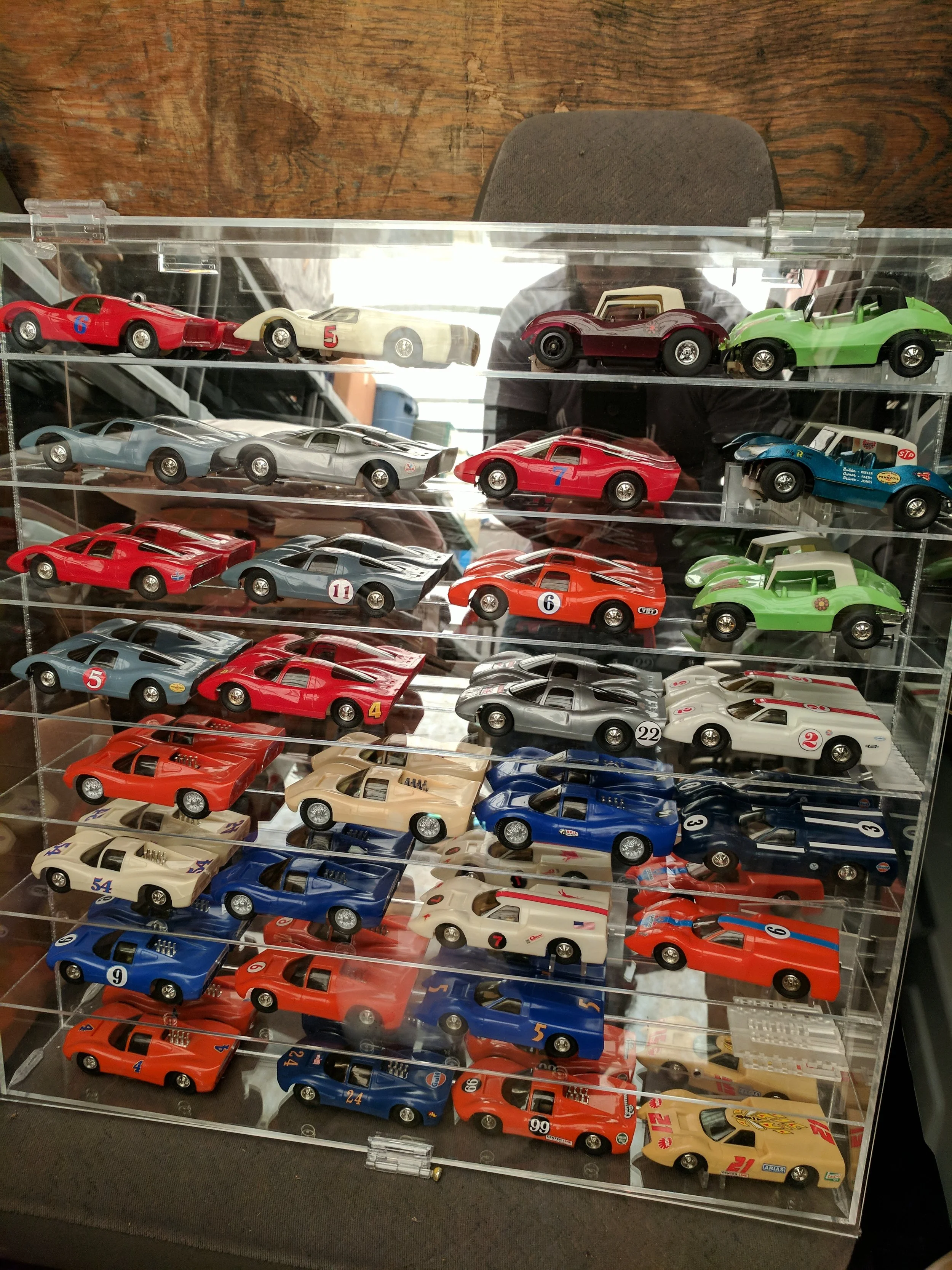 Collection of vintage diecast race cars displayed in a clear plastic case with multiple shelves, featuring various colors and racing numbers.