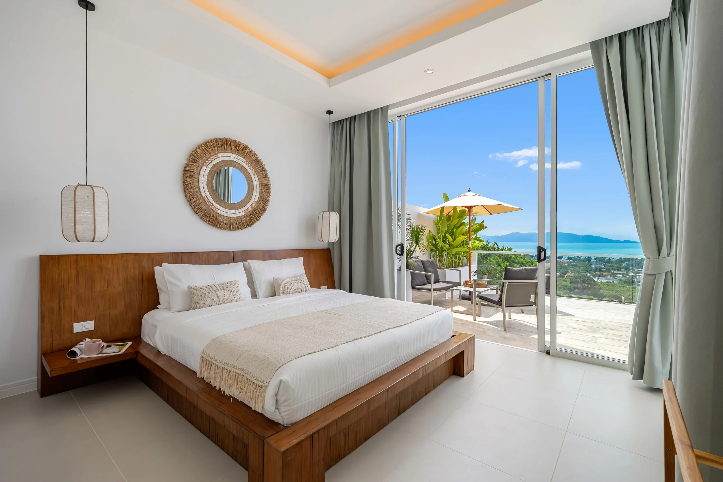 Hotel room with a large bed, balcony with view of ocean and mountains, and modern decor.