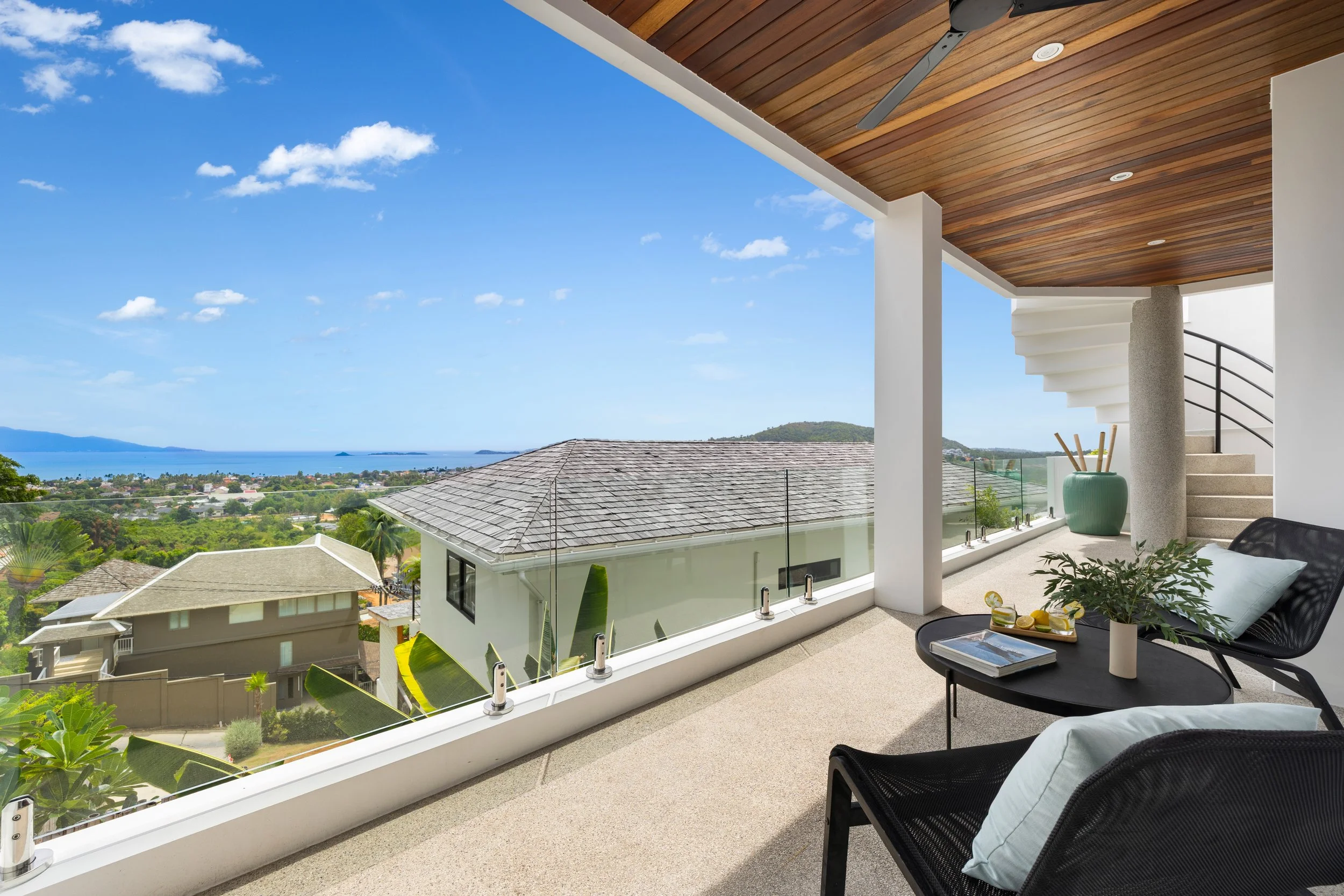 Balcony with outdoor seating, potted plants, and ocean view.