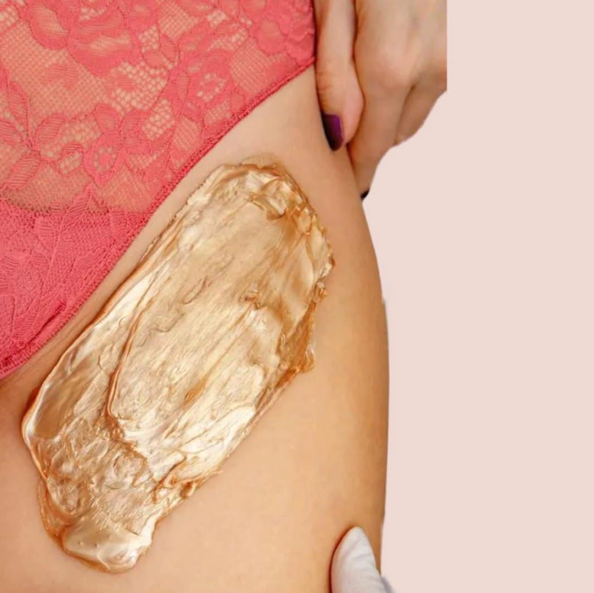 A person applying a large amount of beige body cream or lotion to their thigh, with part of lace pink underwear visible.