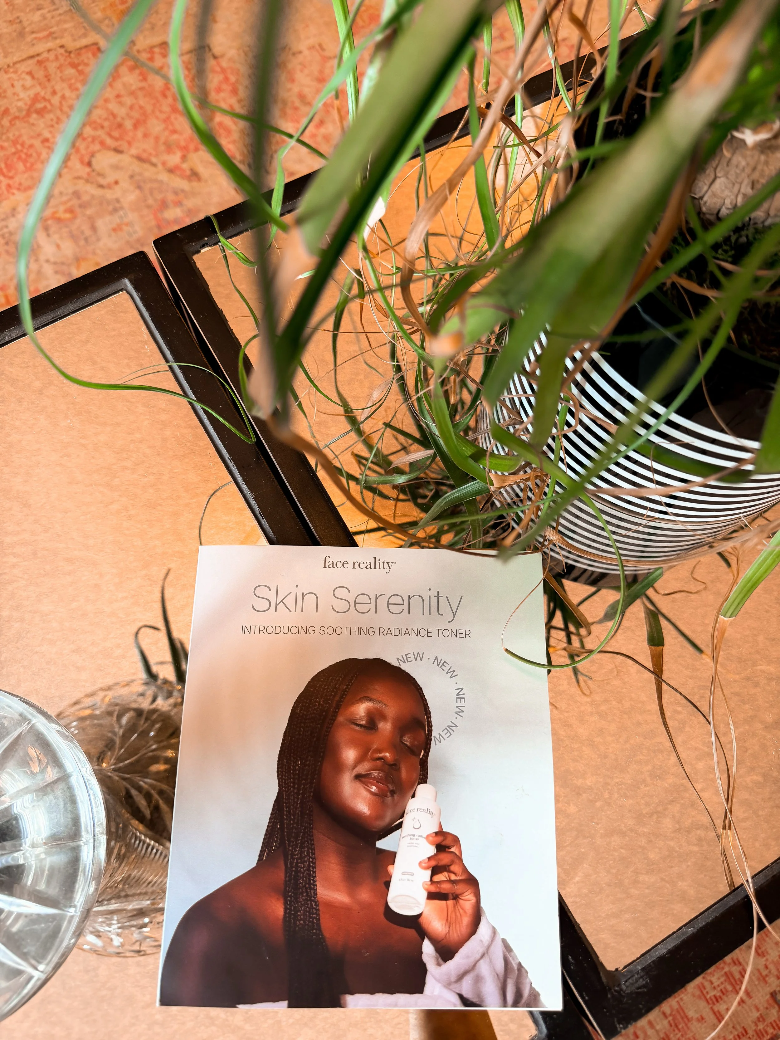 A woman with dark skin and braided hair holding a white bottle of skincare product, smiling with her eyes closed