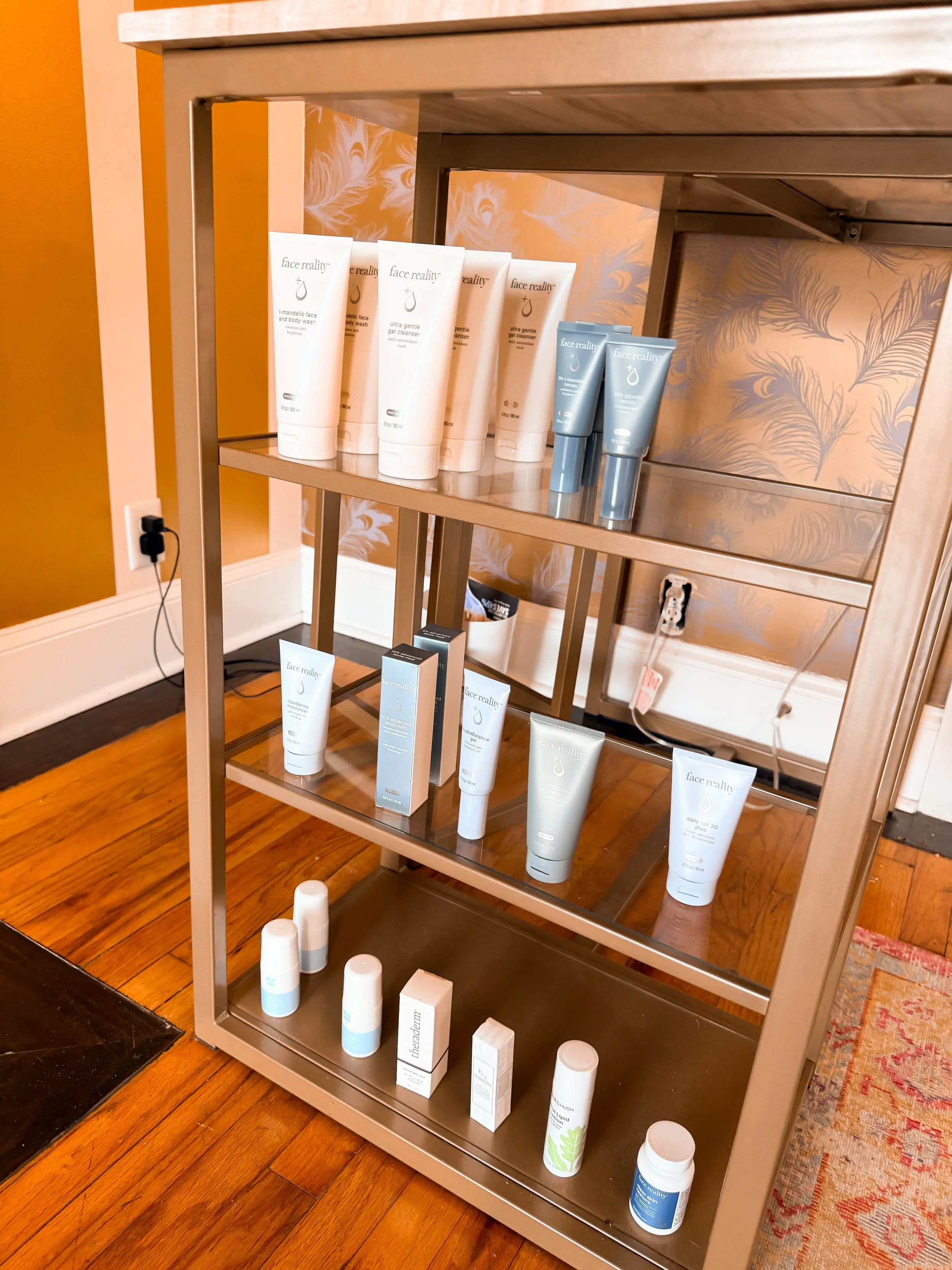 A metal shelf displaying various skincare products including creams and serums in tubes and boxes, with a wooden floor and patterned wallpaper in the background.