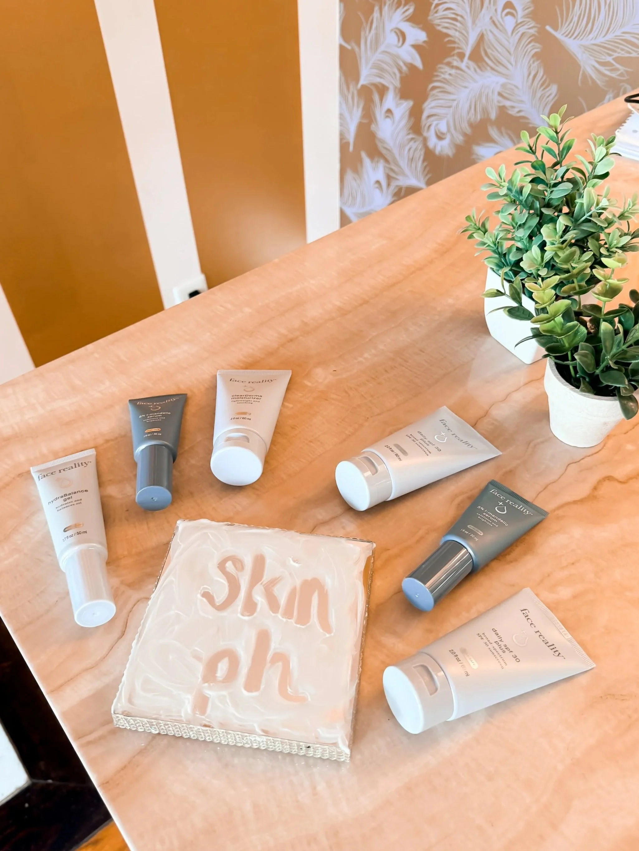 A beige tissue box with a swirling pattern on a wooden table, along with potted green plants and tubes of skincare products labeled 'Face Reality'.