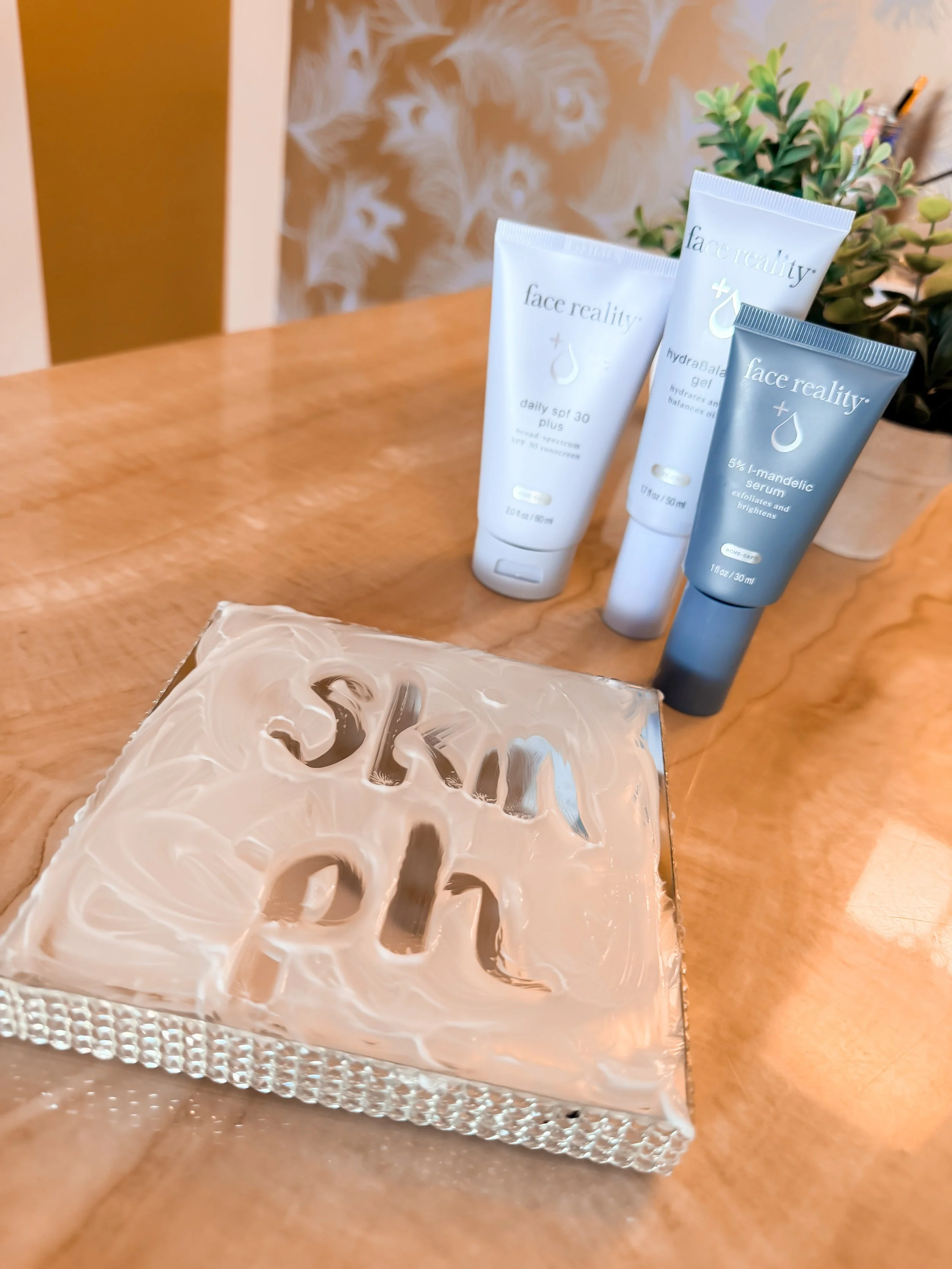 Three tubes of face reality skincare products on a wooden surface with a potted plant in the background.