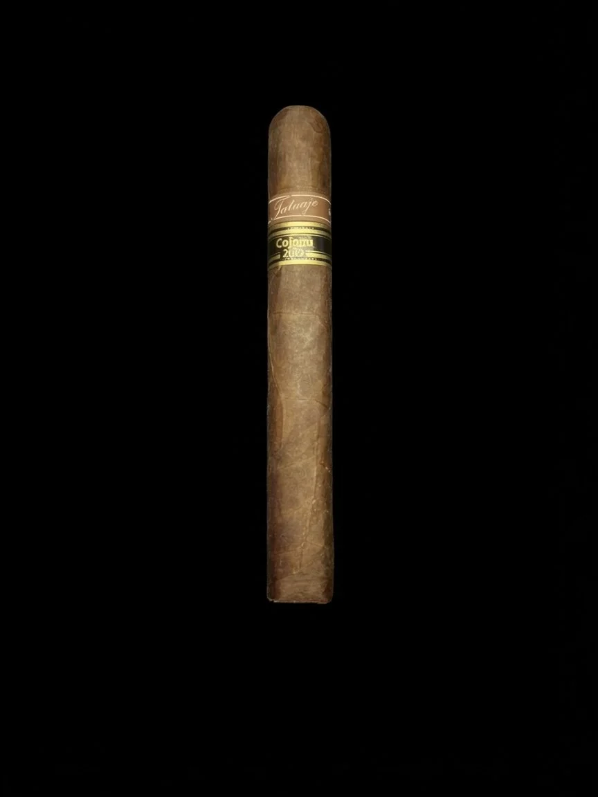 A single cigar with a band that has gold and black details against a black background.