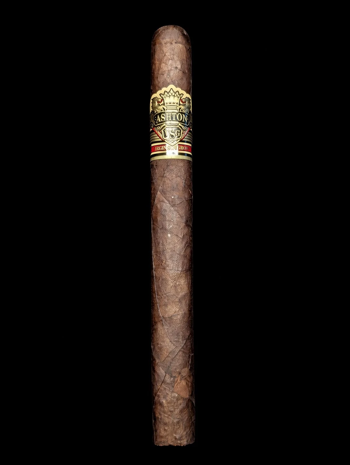 A single brown cigar with ornate gold, black, and red band featuring the text 'ASHETON USG' and a crown.