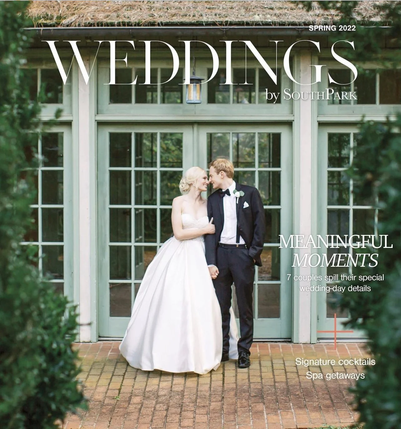 A wedding magazine cover featuring a bride and groom standing close together, looking at each other and smiling, outside a greenhouse-style building with large windows, surrounded by greenery.