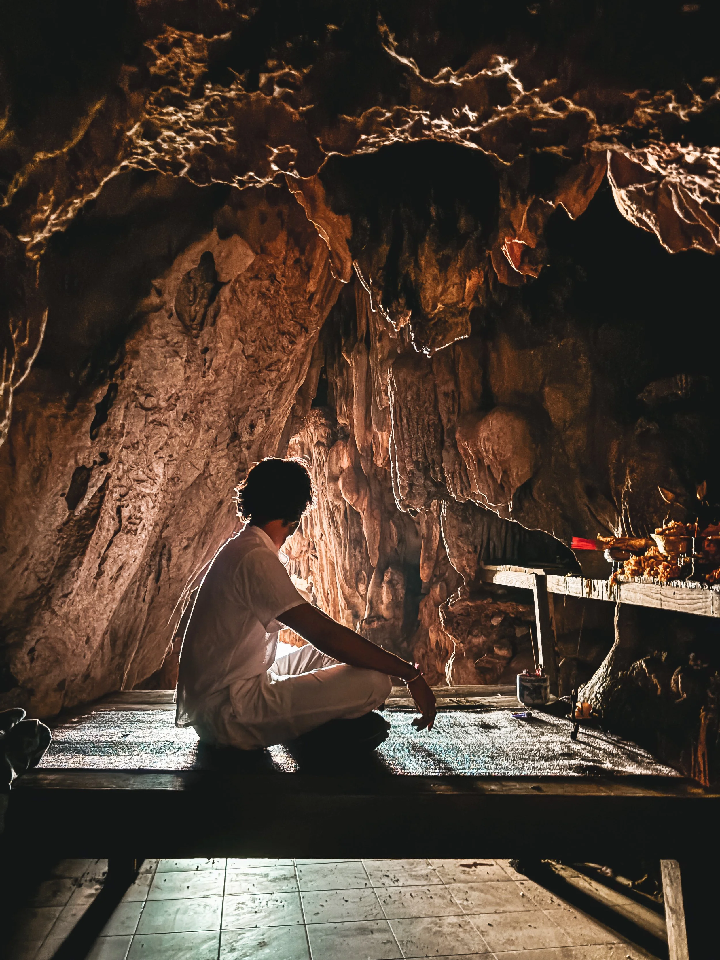 Person practicing meditation or yoga inside a cave with natural rock formations, sitting cross-legged on the ground with their eyes closed.