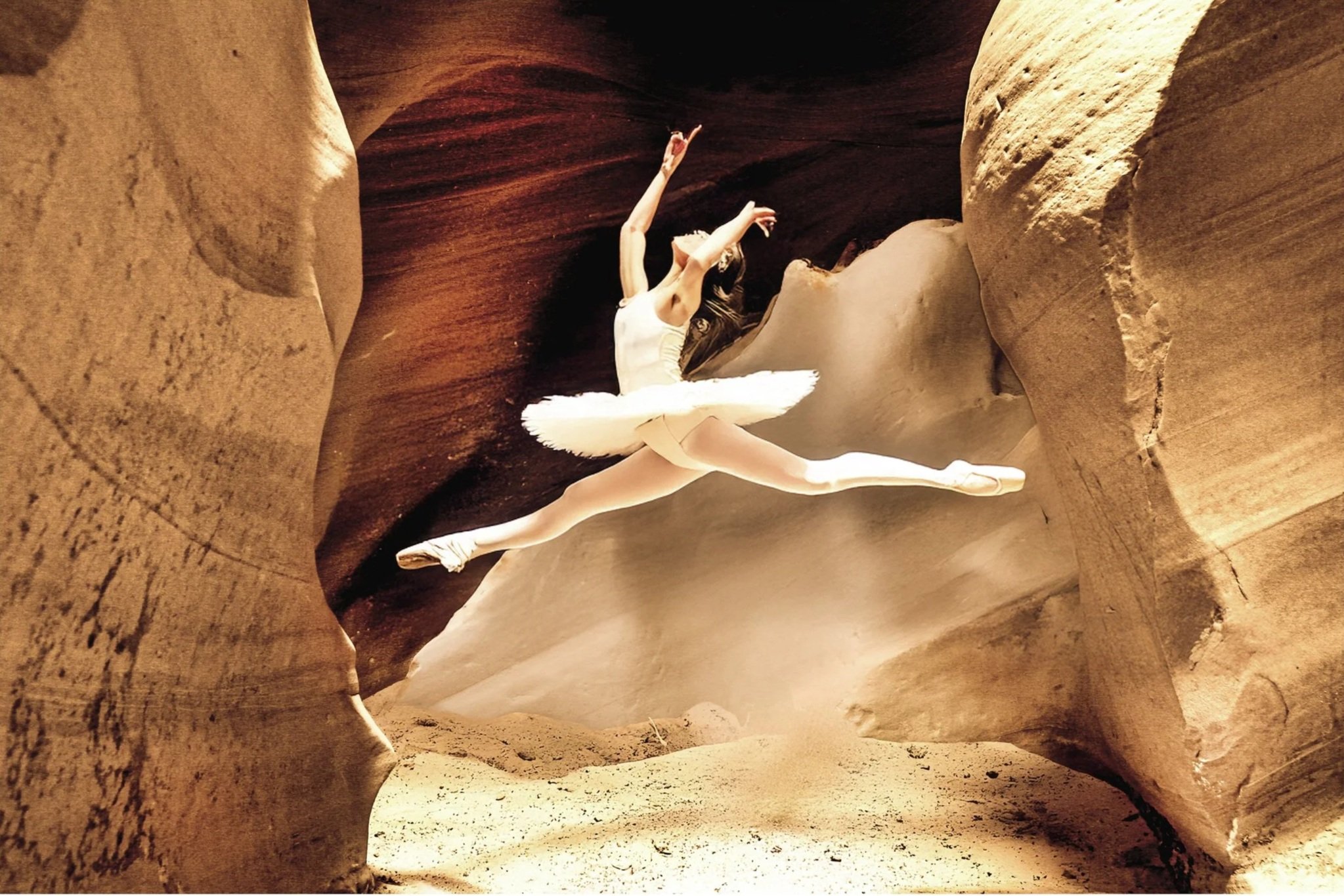 A ballet dancer in a tutu performing a grand jeté inside a narrow, winding sandstone canyon.
