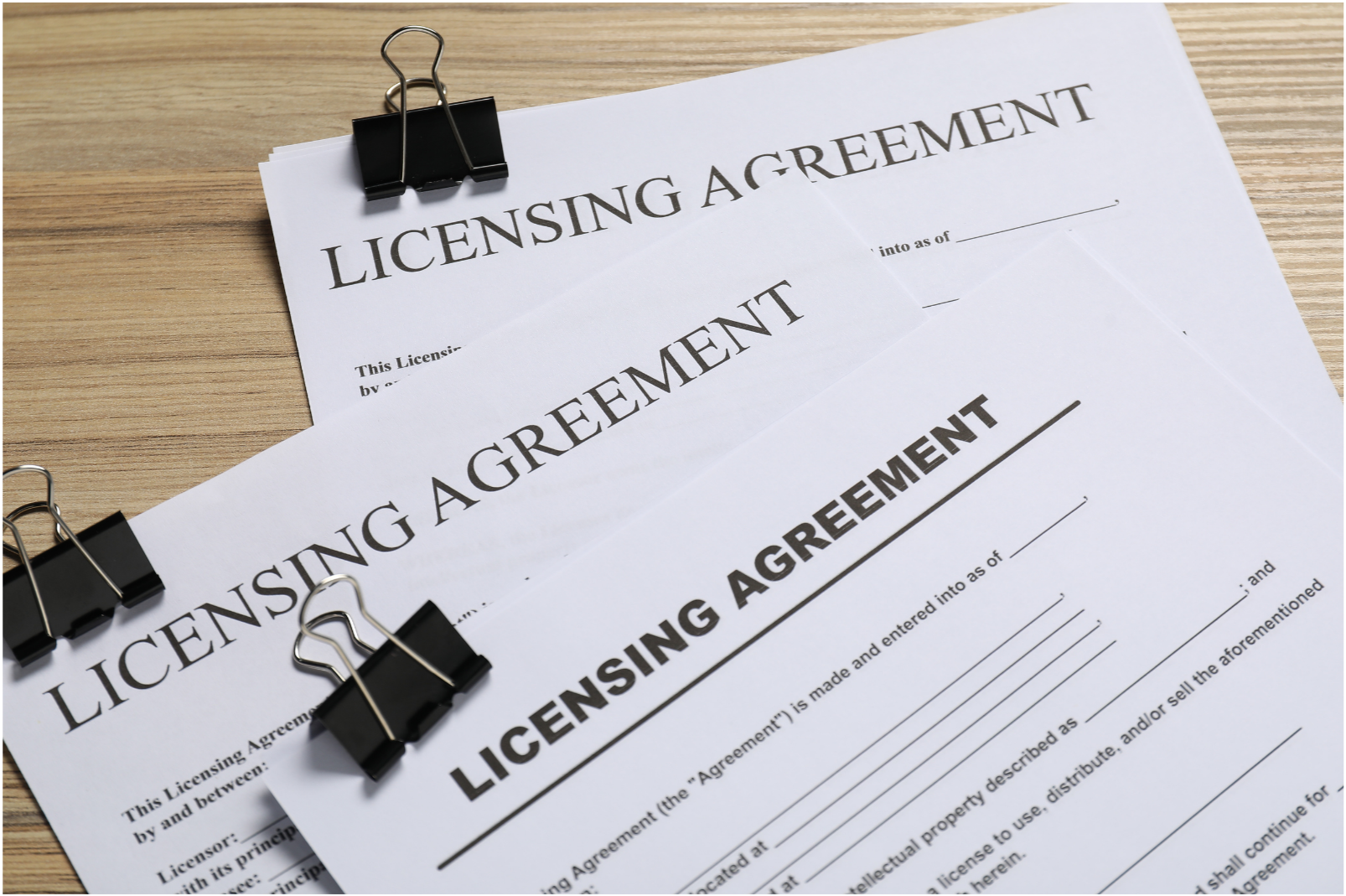 Multiple copies of a licensing agreement document clipped with black binder clips, placed on a wooden surface.