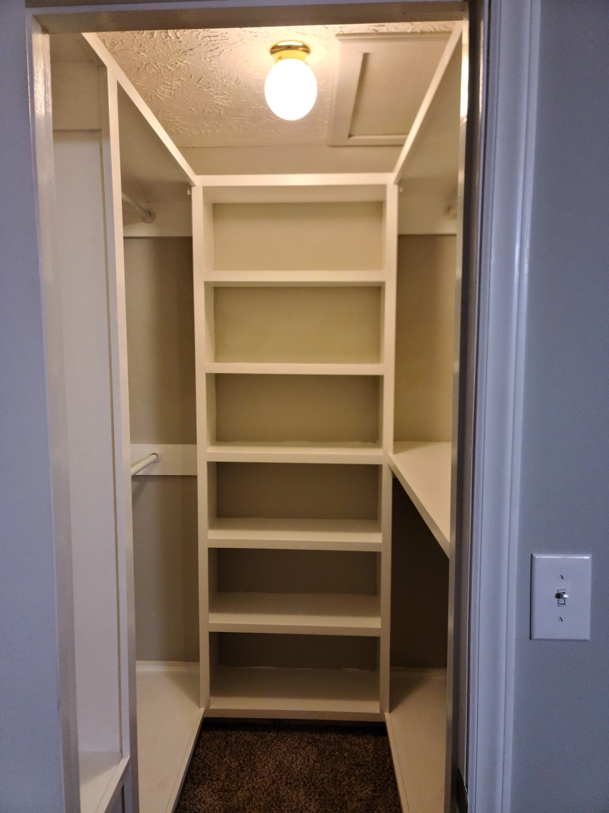 Empty walk-in closet with white shelving, a hanging rod on the left, and a light fixture on the ceiling.