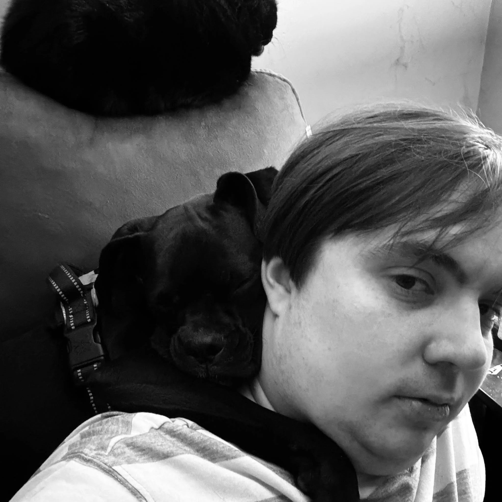 Black-and-white photo of a person lying on a bed, partially visible, with a focus on their hair, skin, and clothing. The person is resting with their head on a pillow, and the image is taken from an angle that shows part of their face and shoulder.