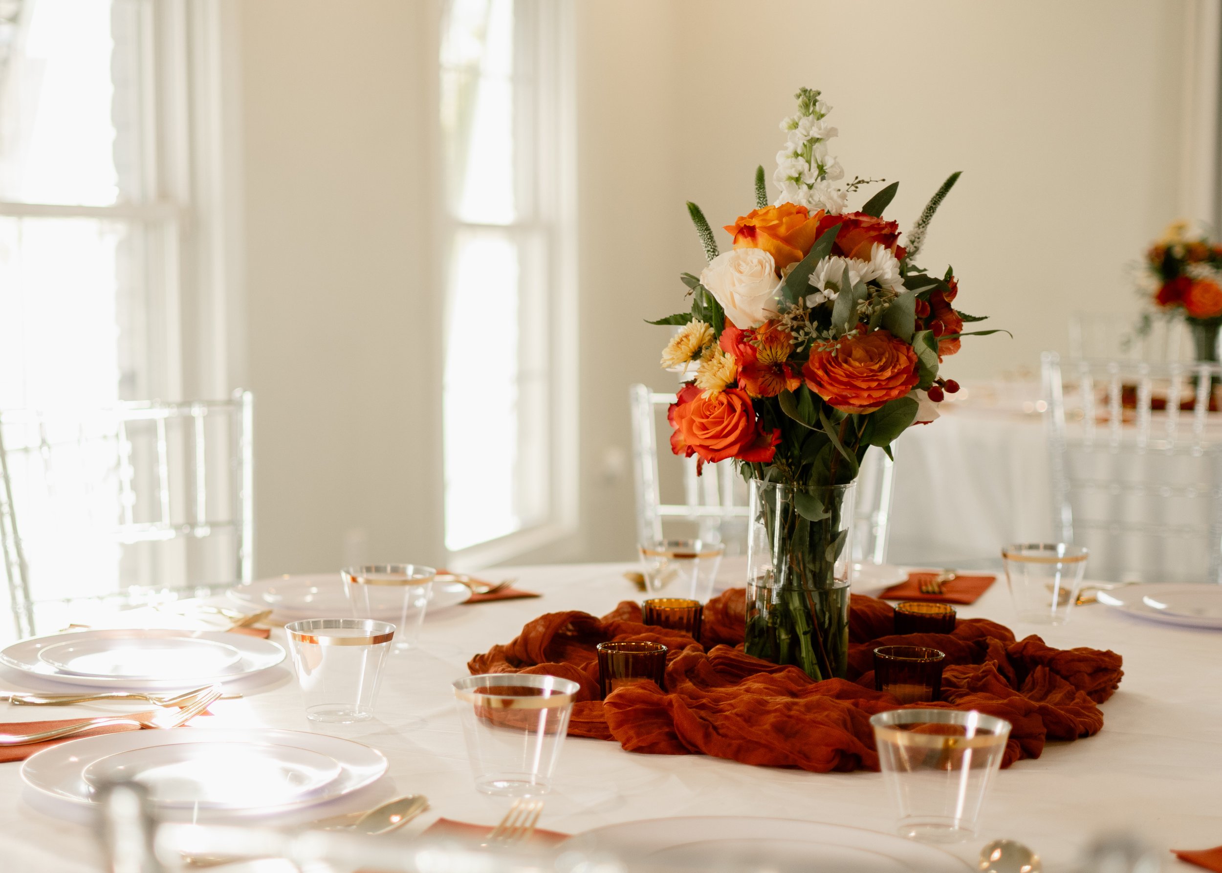 A floral centerpiece with orange and white roses, white snapdragons, and green foliage on a decorated table for a formal event.