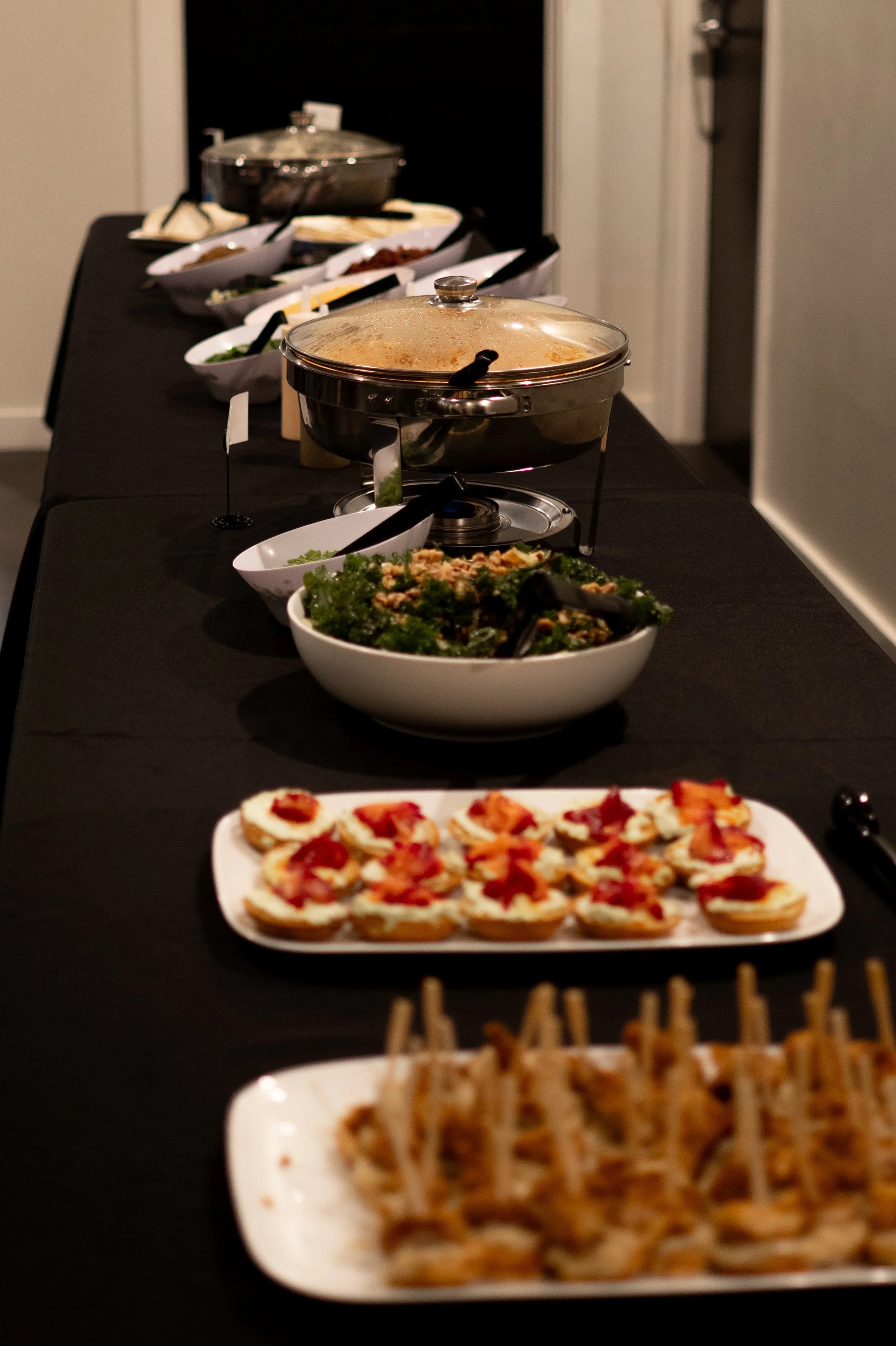 A buffet table with various dishes including pizza slices, salad, cooked vegetables, and cooked meats, set up in a formal dining environment.