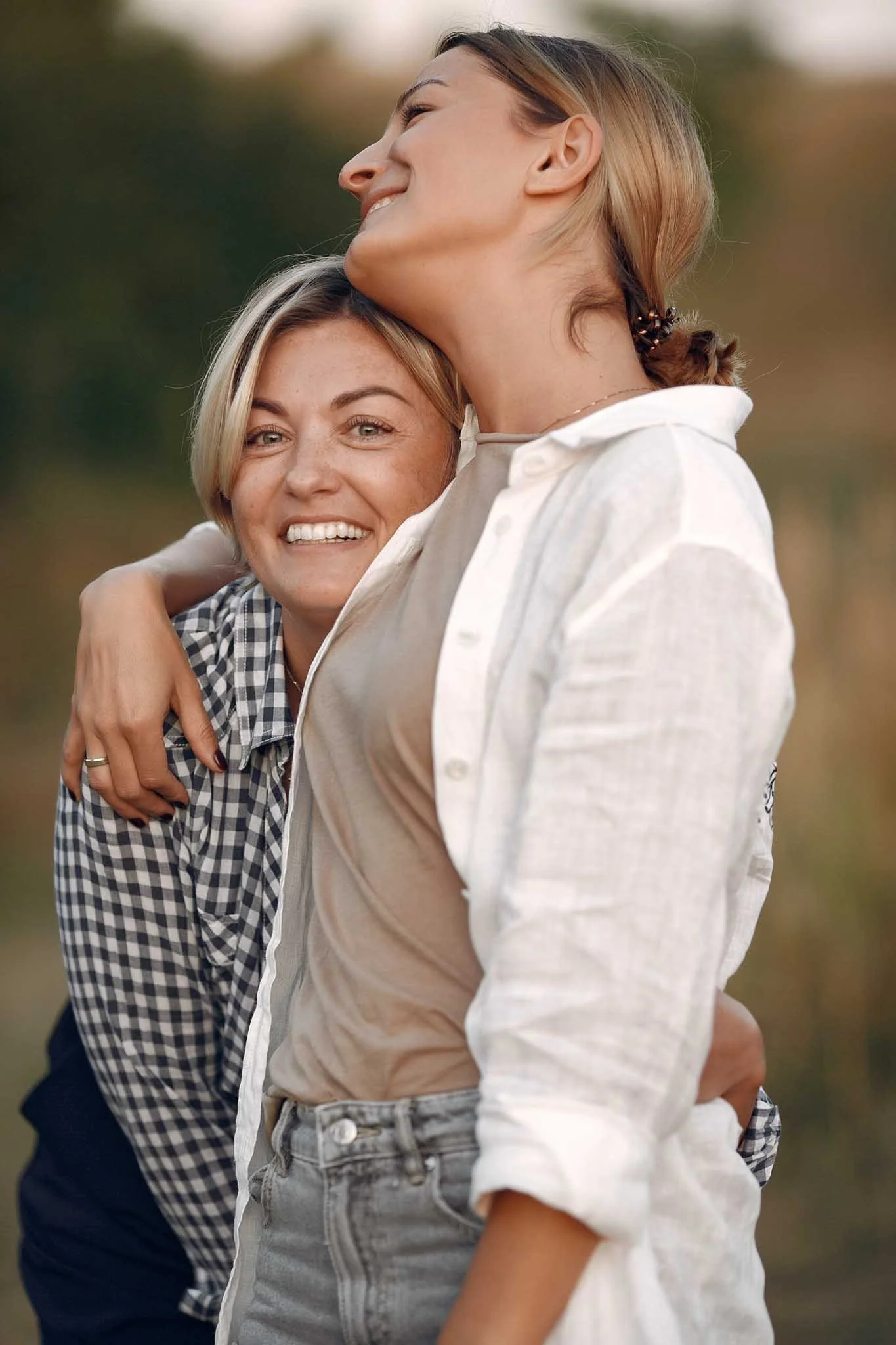 Two women hugging outdoors, smiling and enjoying time together during what appears to be sunset or early evening.