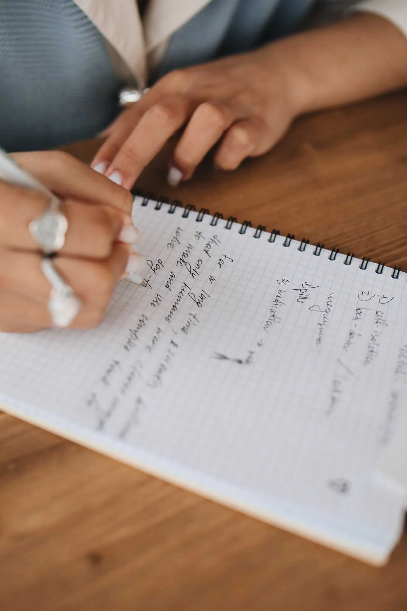 Close-up of a person writing in a notebook with grid paper, on a wooden surface, with visible handwriting.