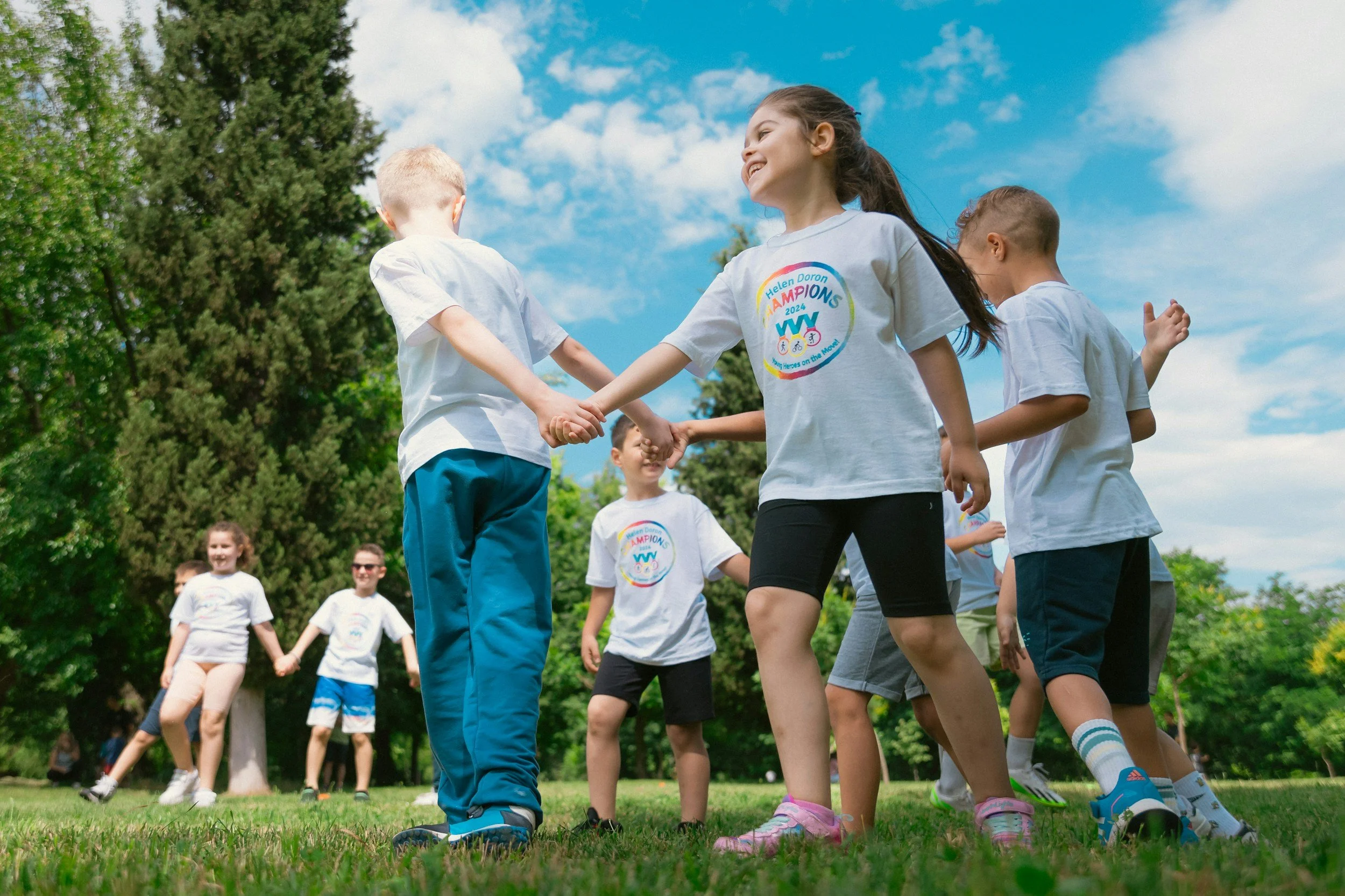 Children holding hands in a circle outdoors on a sunny day, smiling and playing.