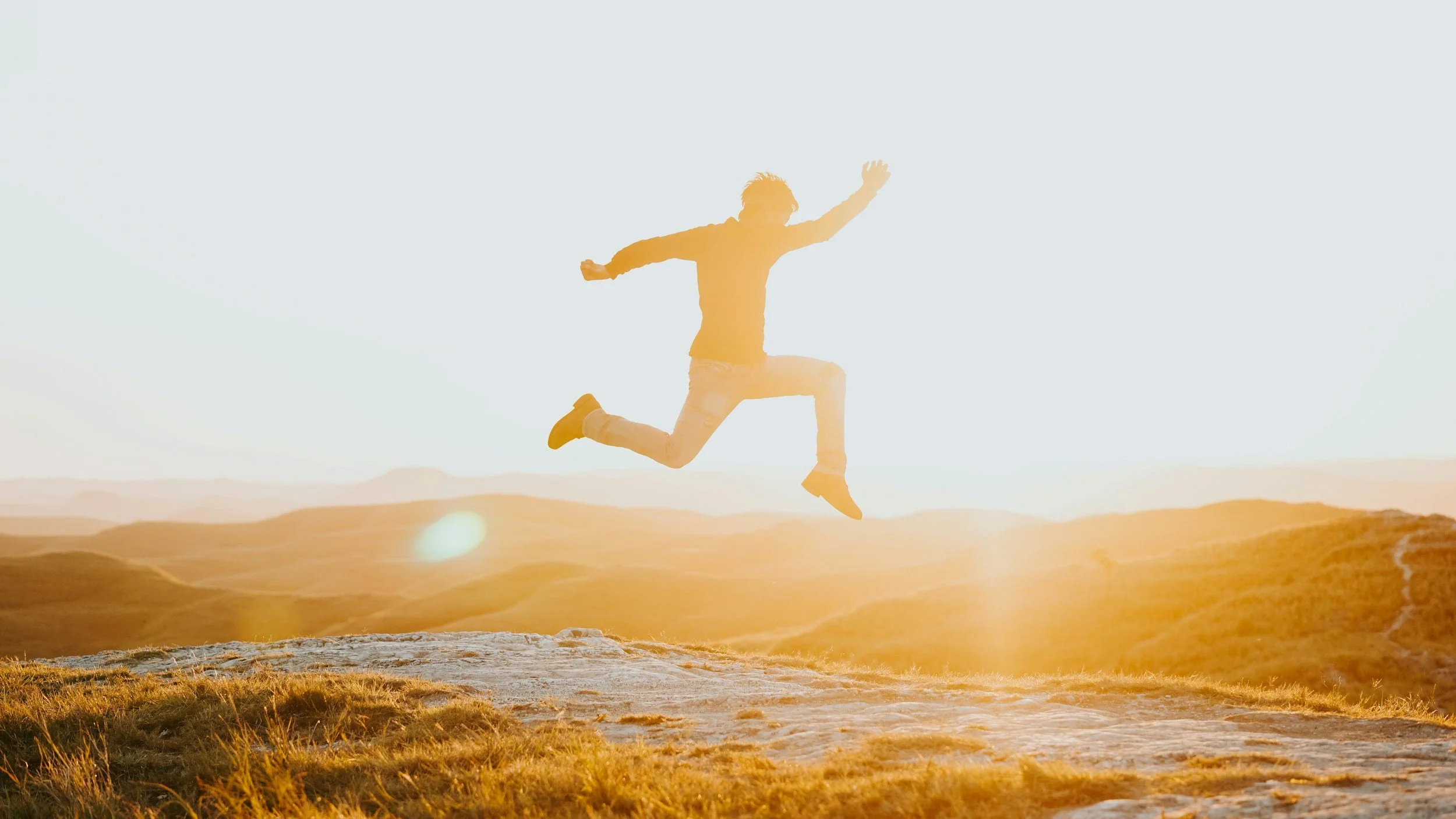 A person jumping in the air during sunset in an outdoor landscape.