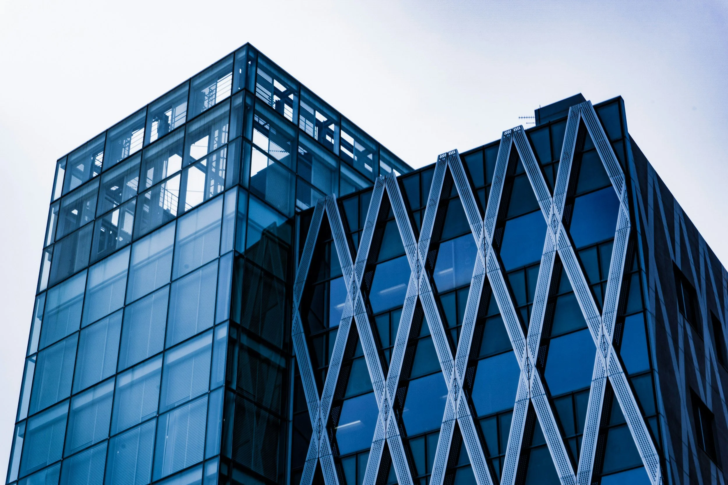 A modern glass skyscraper with geometric architectural design, featuring reflective blue-tinted windows and decorative vertical elements against a cloudy sky.