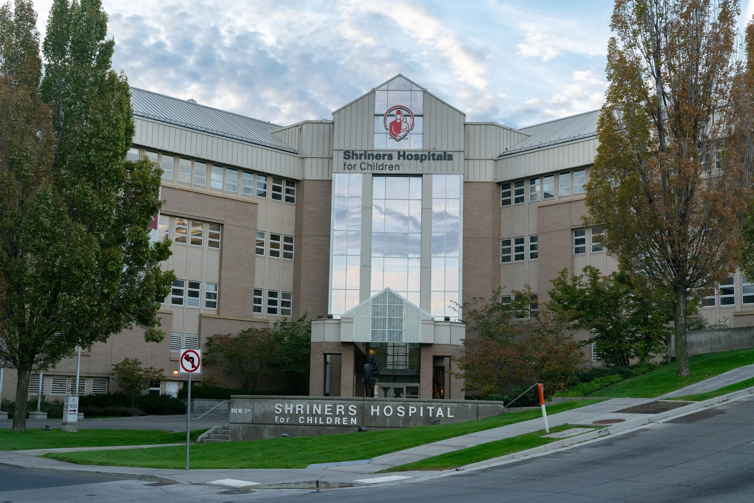 Facade of Shriners Hospitals for Children building with trees and a sidewalk in front.