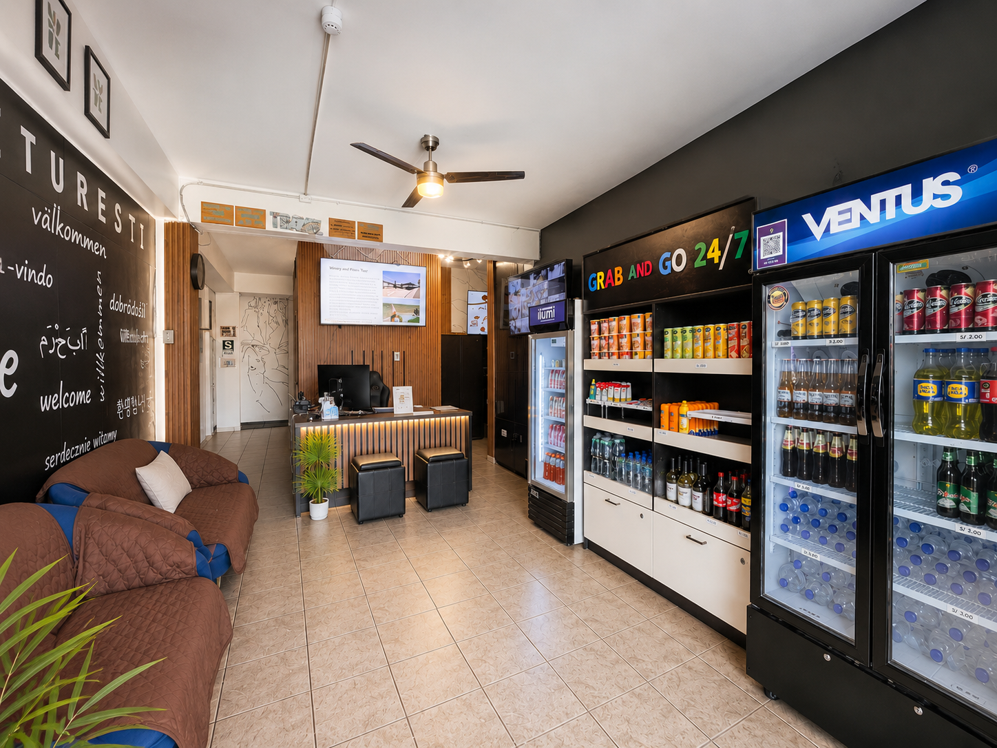 Interior of a small convenience store with a check-in counter, seating area, vending machines, and shelves stocked with drinks and snacks.