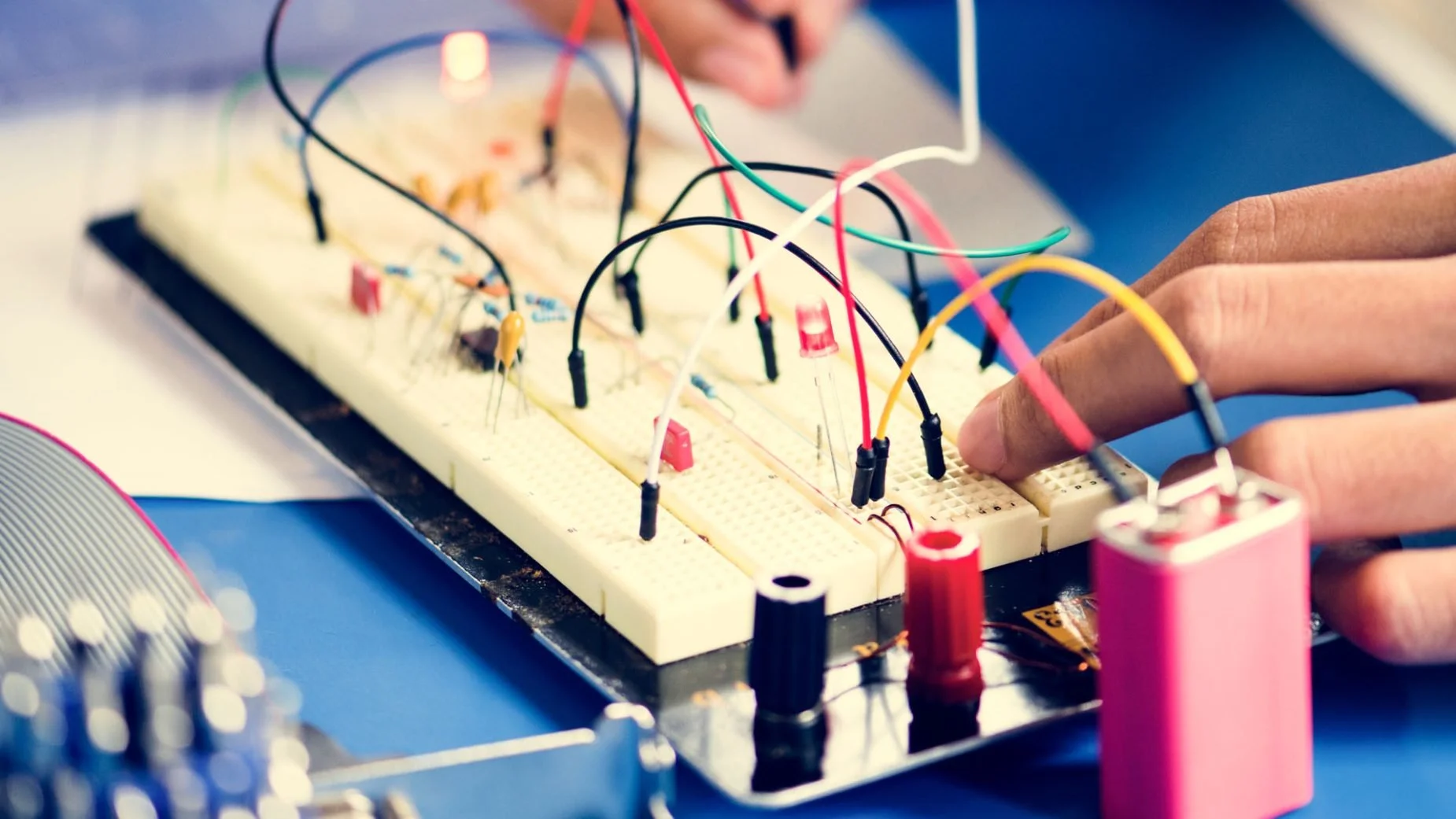 Close-up of a breadboard with colorful electrical wires and electronic components, and a person's fingers adjusting the wiring, suggesting an electronics project or experiment.