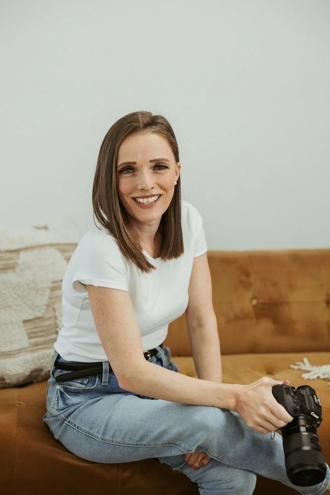 Hannah Cummins seated on a leather couch, smiling, camera in hand