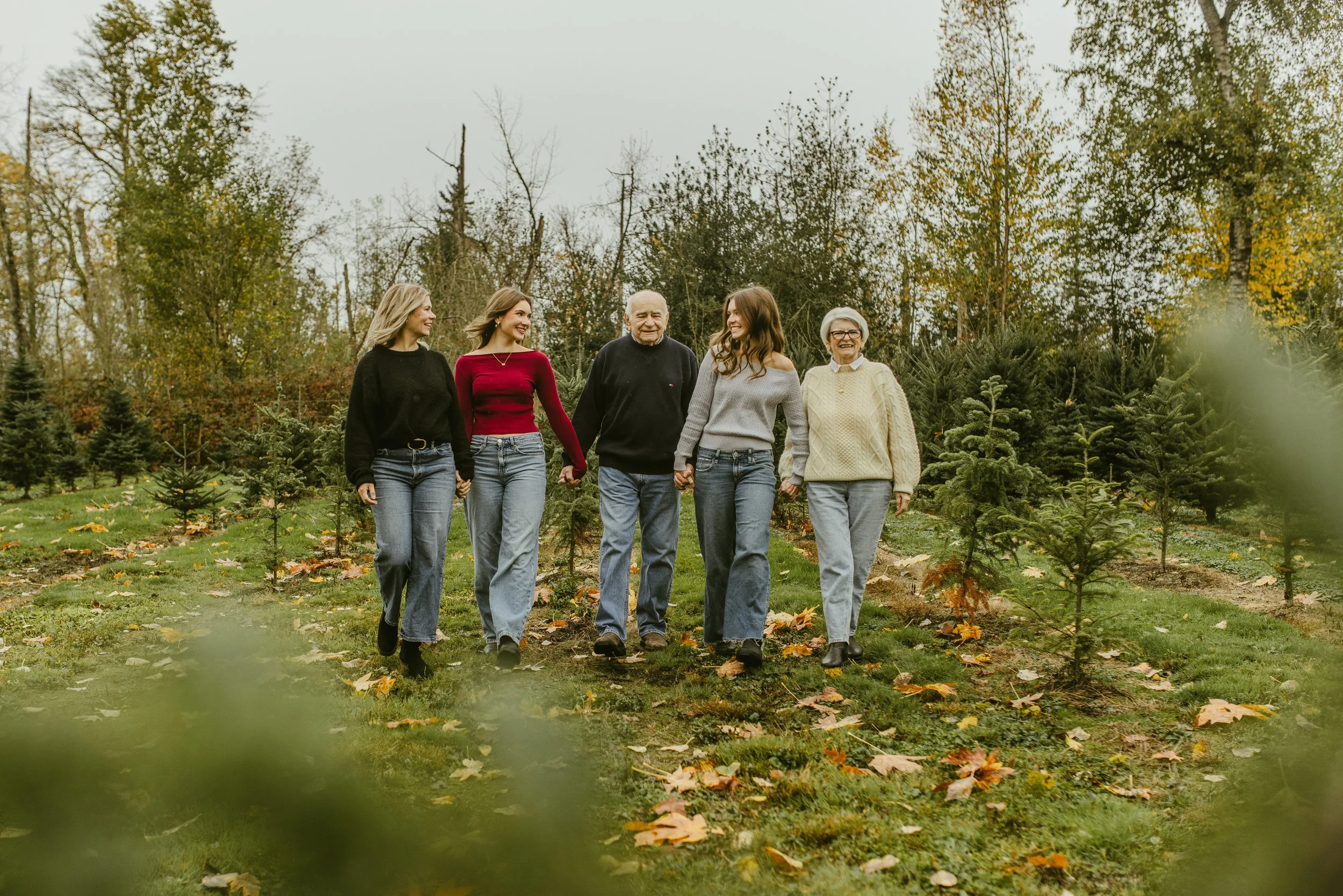 Extended family walking hand in hand through a Christmas tree farm