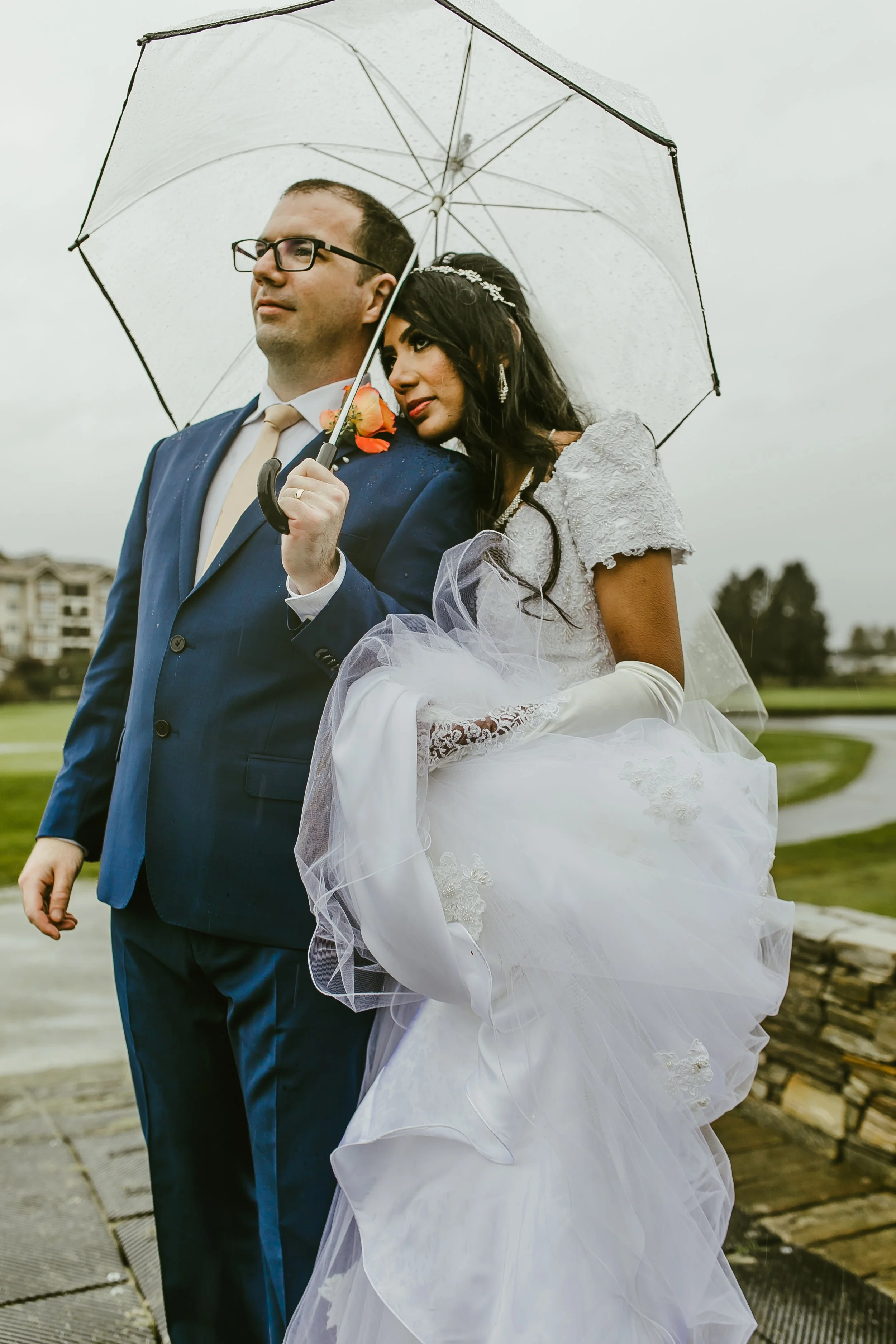 Newlyweds sheltering under a white umbrella on a rainy wedding day