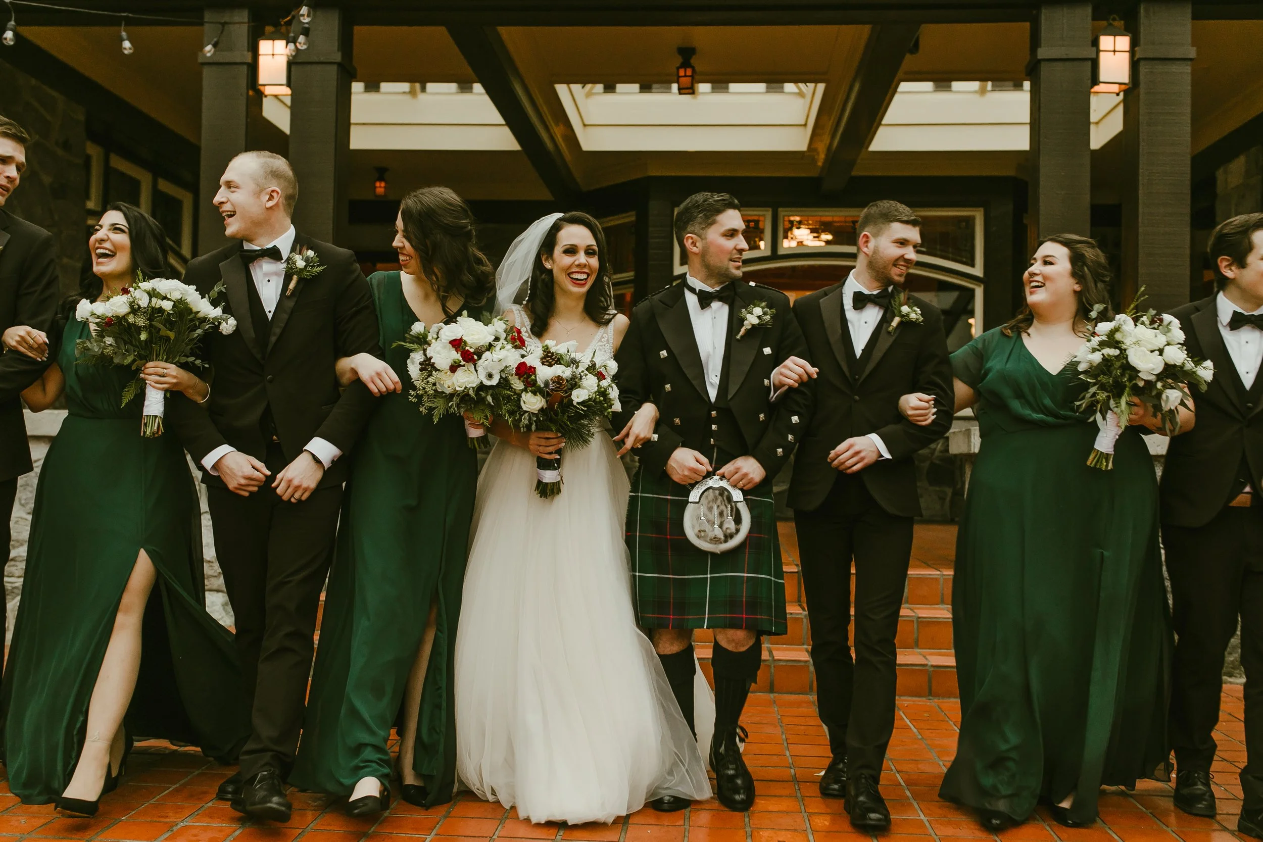 Wedding party in forest green walking arm in arm at the reception