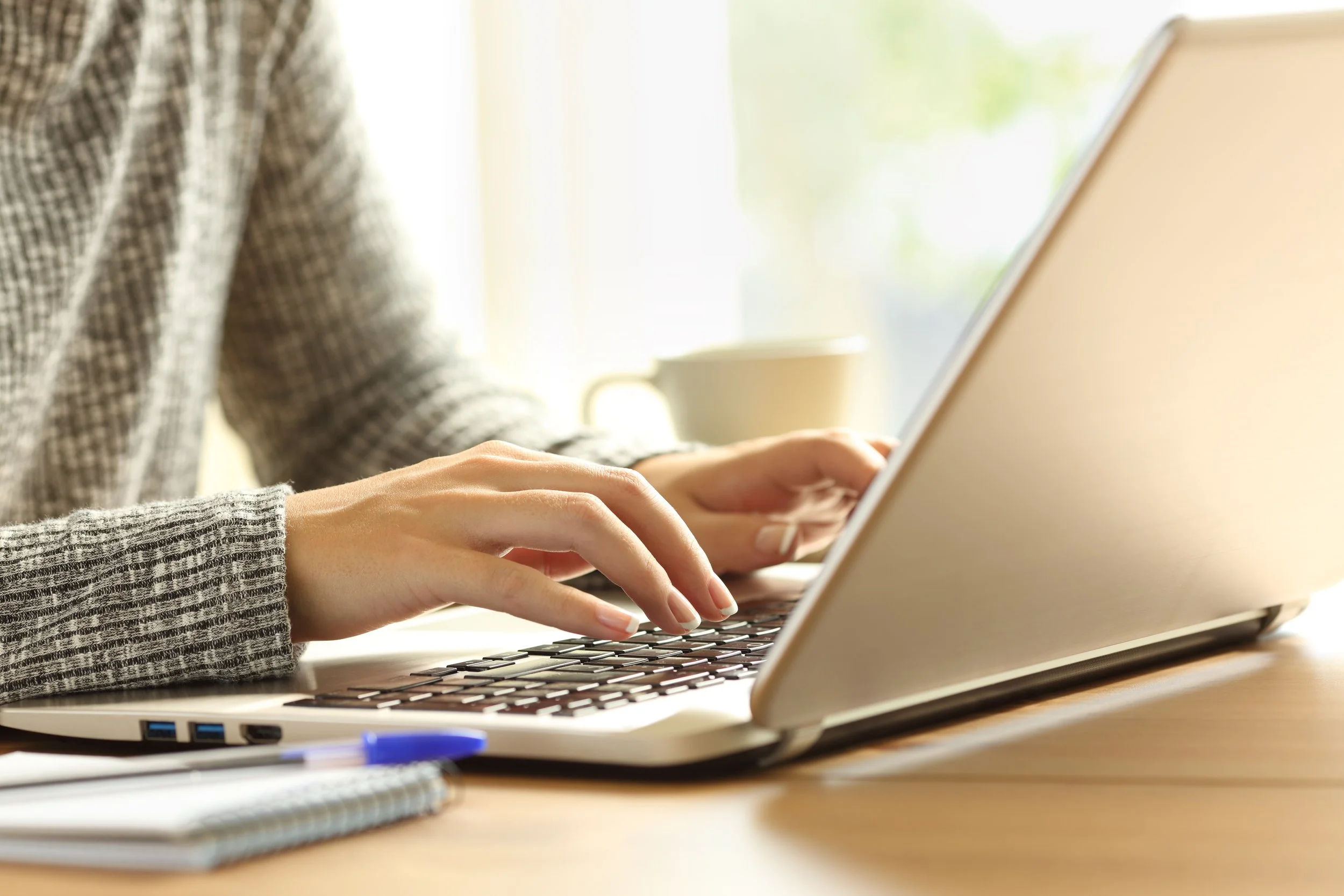 Woman typing on a laptop at a desk with notebooks and a pen.