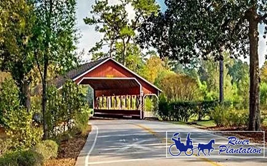 River Plantation community entrance - rural covered bridge over a small road, surrounded by trees and greenery.