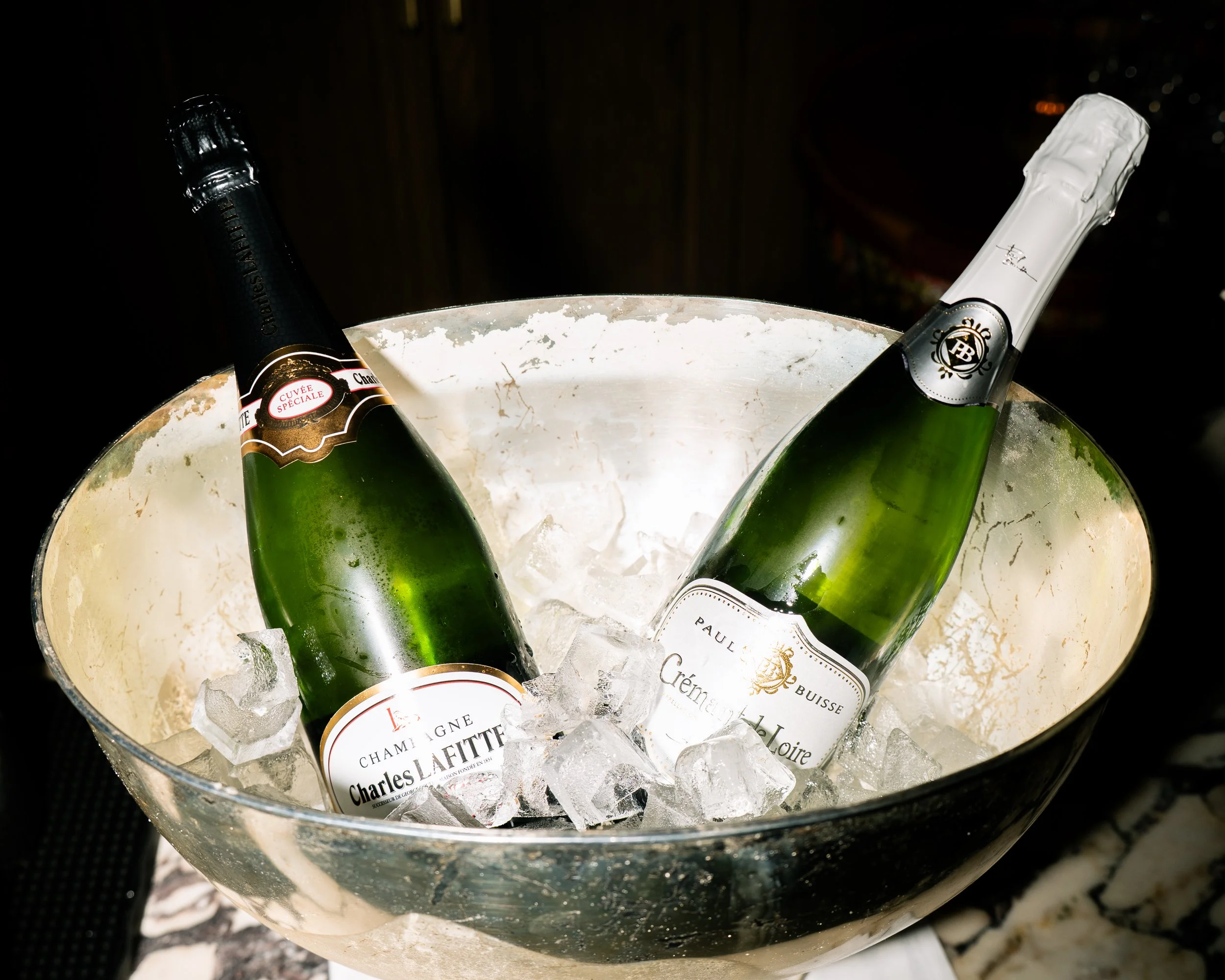 A silver ice bucket containing three bottles of champagne with labels visible, surrounded by ice cubes.