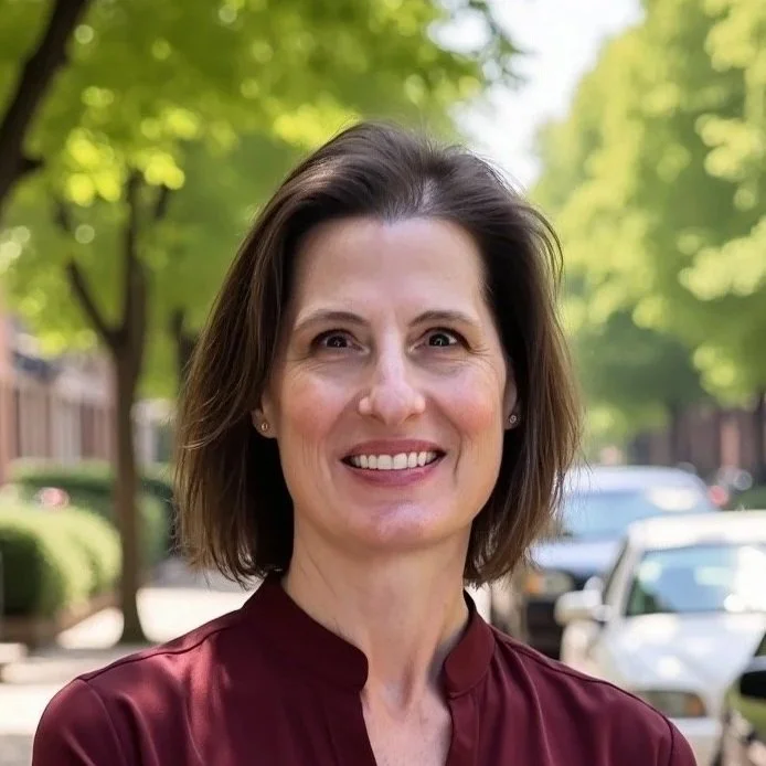 A woman with shoulder-length brown hair smiling outdoors on a sunny day.