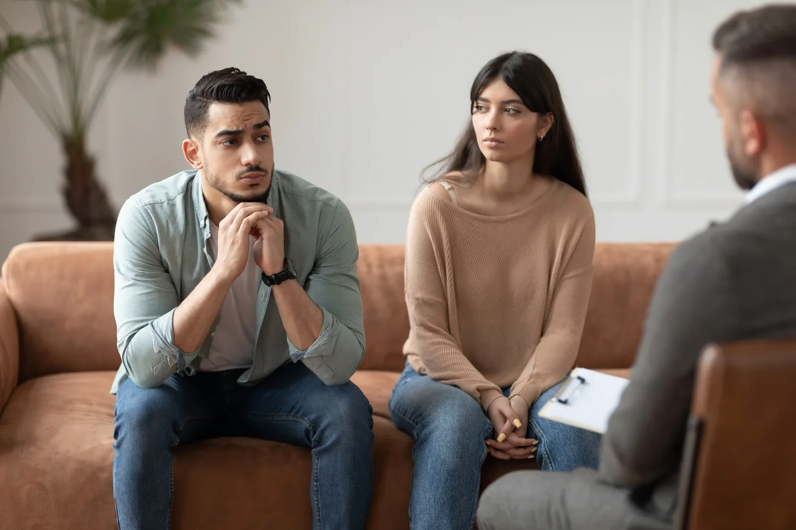 A young man and woman sitting on a sofa during a counseling session with a therapist.