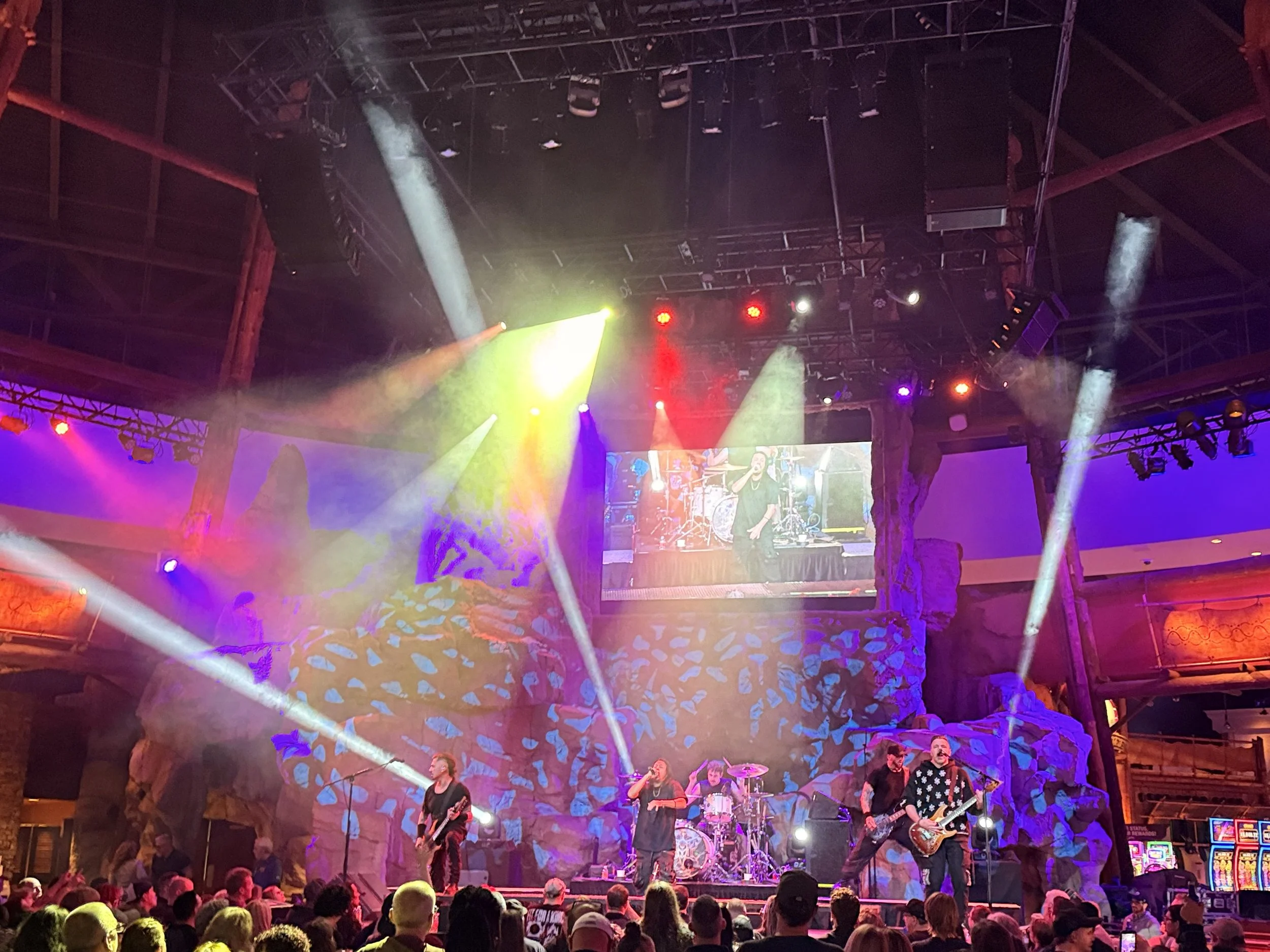 A live music performance on stage with band members playing instruments, surrounded by colorful stage lights and an audience in front.