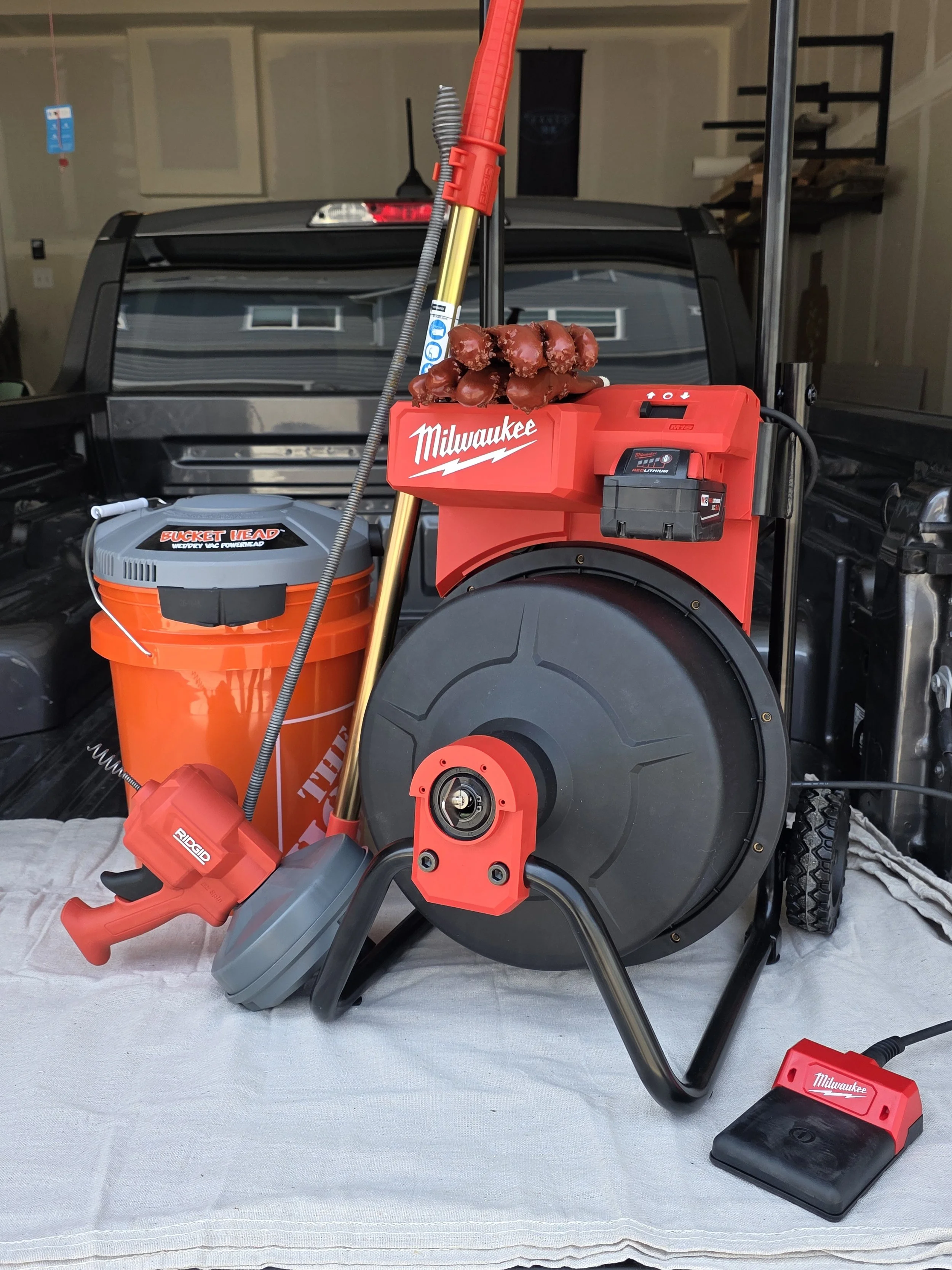 Power tool setup with a Milwaukee cordless drill, a large surface with a coil of chocolate candies, and a shop vacuum, all arranged on a white cloth in a garage.