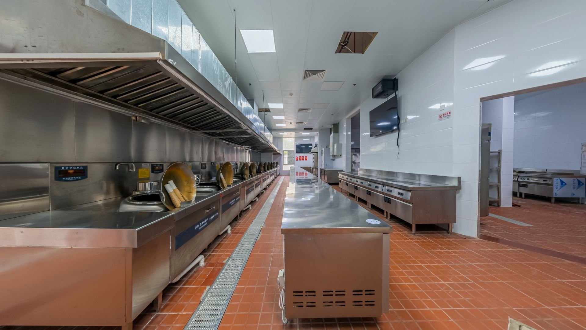 Empty commercial kitchen with stainless steel appliances, large cooking stations, and tiled floors.