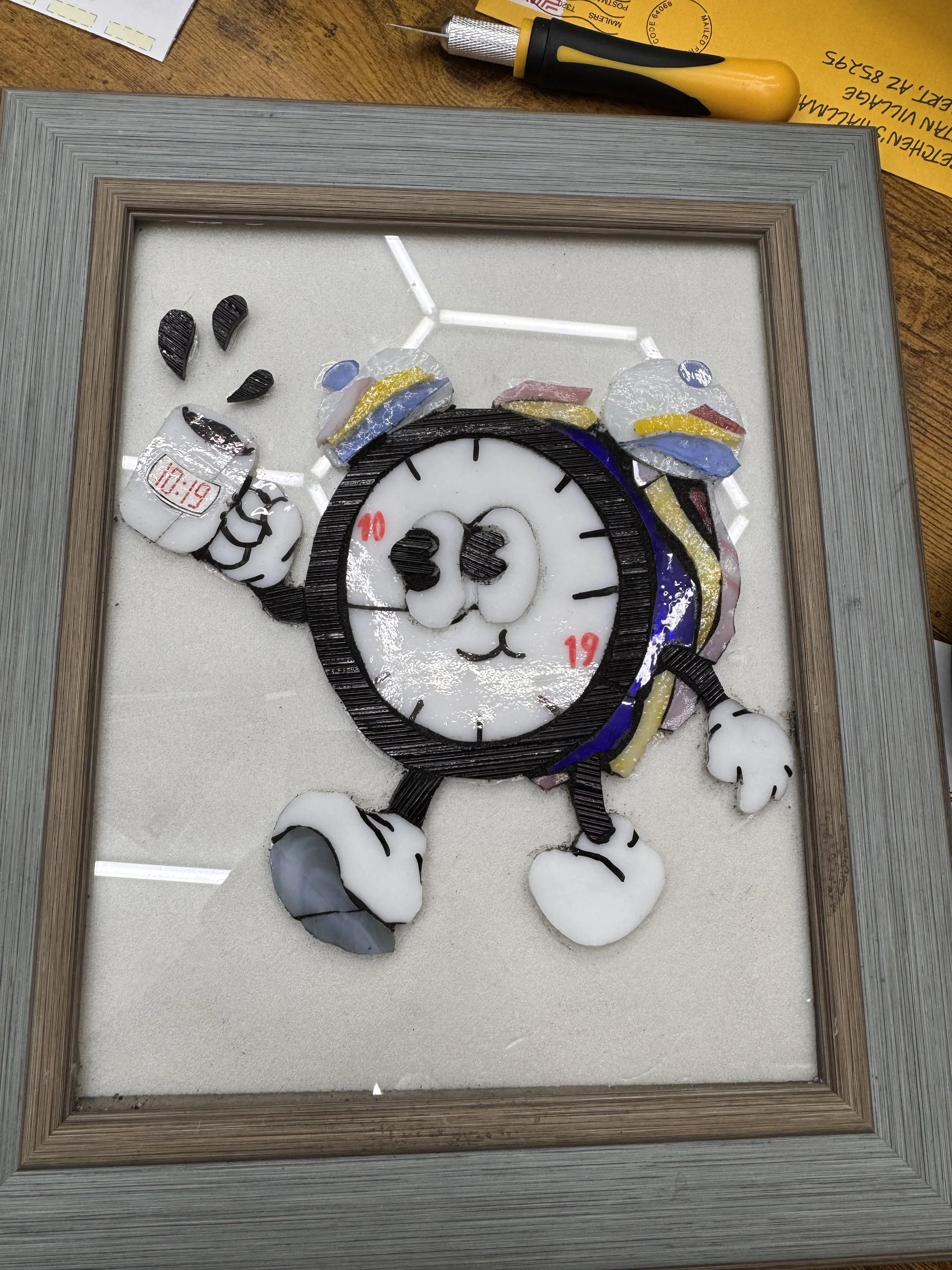 A mosaic art piece of Mickey Mouse, created with colored glass and tiles, displayed in a wooden frame on a table.