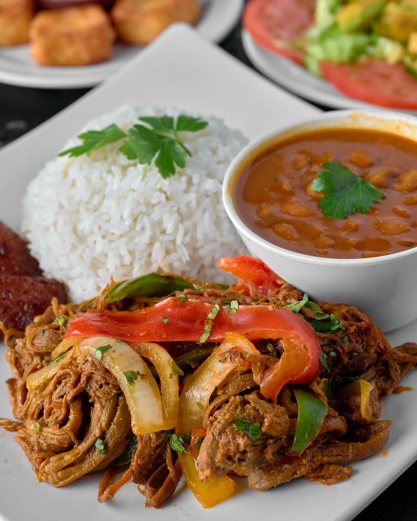 Plate of Indian cuisine featuring shredded chicken curry with vegetables, white rice topped with parsley, and a bowl of chickpea curry garnished with parsley.
