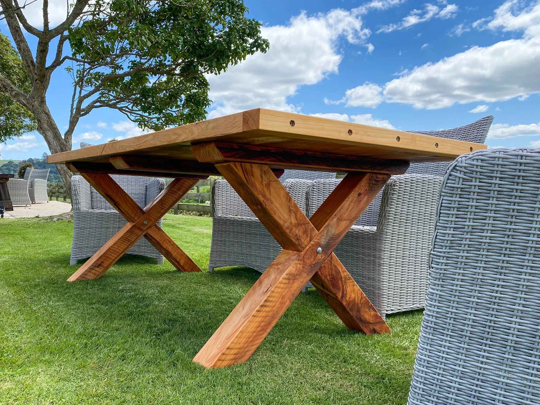 Macrocarpa dining table with distinctive X-shaped timber legs in an outdoor setting.