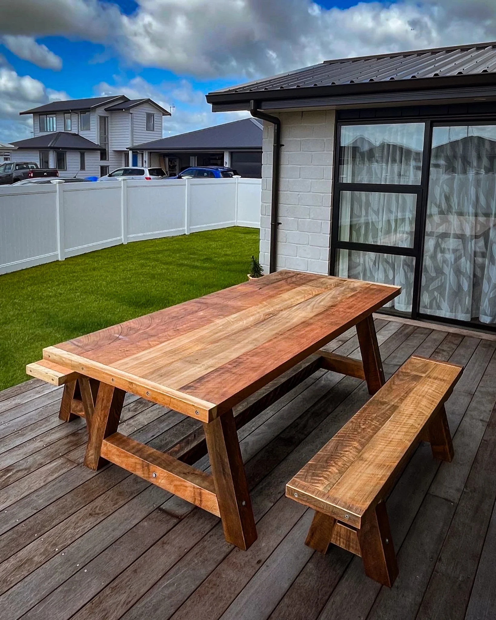 Macrocarpa dining table with matching bench seats on a residential deck.