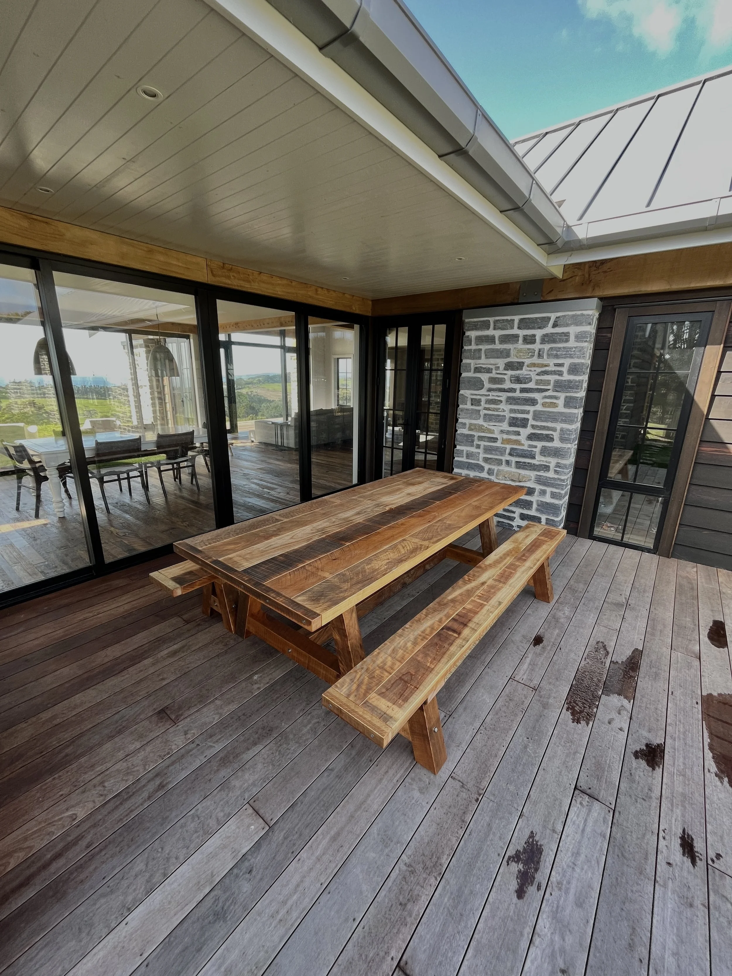Macrocarpa dining table with matching benches in a covered outdoor living area.