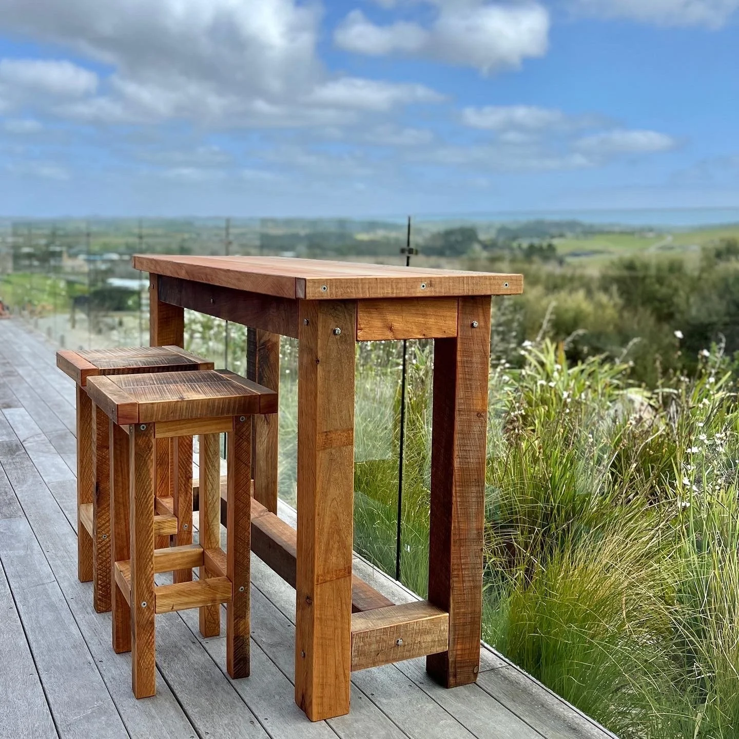 Macrocarpa bar leaner with matching timber stools on an outdoor deck.